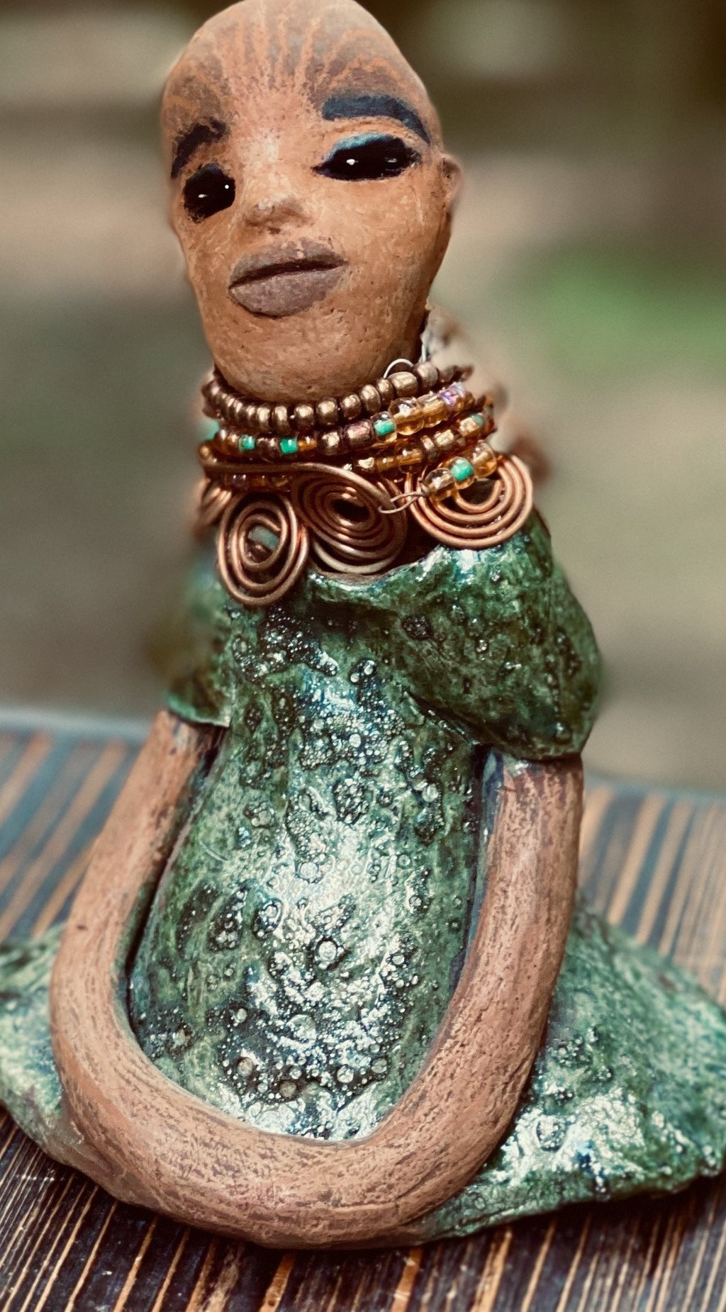 Meet Faye! Faye stands 7" x 5" x 4" and weighs 2.3 lbs. She has a lovely two tone honey brown complexion with  chocolate brown lips. She has a braided hairstyle.  Faye has a colorful metallic green antique glazed dress. She wears an awesome beaded collar with a copper spiral necklace. Her long loving arms rest at her side. With eyes wide opened, Faye has hopes of finding a new home.