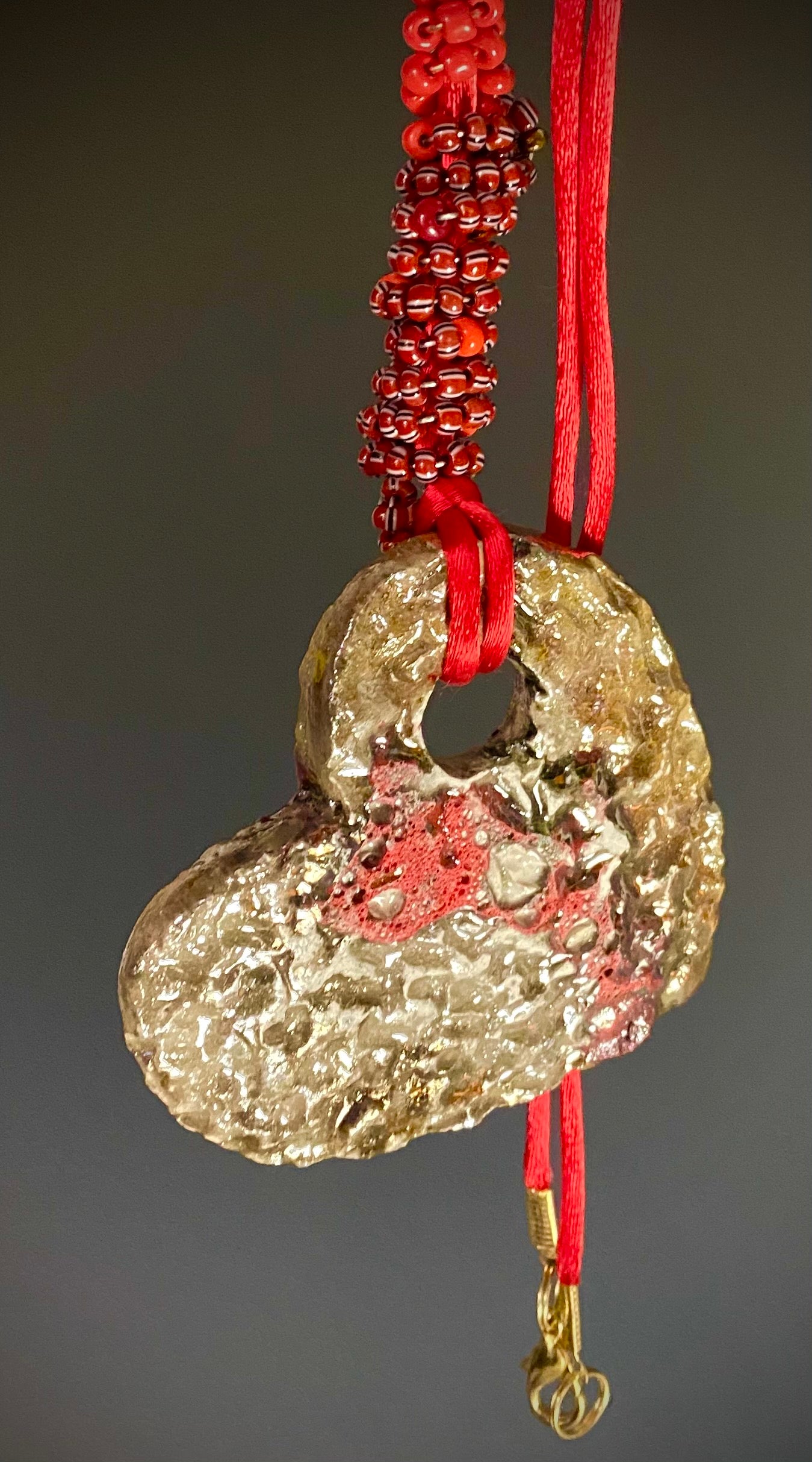 Have A Heart! Each heart pendant is handmade with love! It is 3"x 3"and weighs approx. 3ozs. This pendant has a red, white, and gold metallic raku glazes that renders a unique translucent  patina. The heart has a textured pattern . Both sides are  are different and equally beautiful! It holds a spiral of red and deep purple mini beads on a spiral copper wire. This pendant has a nice 12" red adjustable rattail cord!