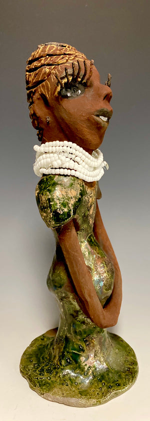 Meet Erma! Erma stands 11.5" x 5" x 5" and weighs 2 lbs. She has a lovely dark brown complexion with brown lips. She has a braided hairstyle.  Erma has a colorful metallic green antique copper glazed dress. She wears a bright white beaded necklace. With long lashes and eyes wide opened and ultra white teeth, Erma has hopes of finding her way into your home!