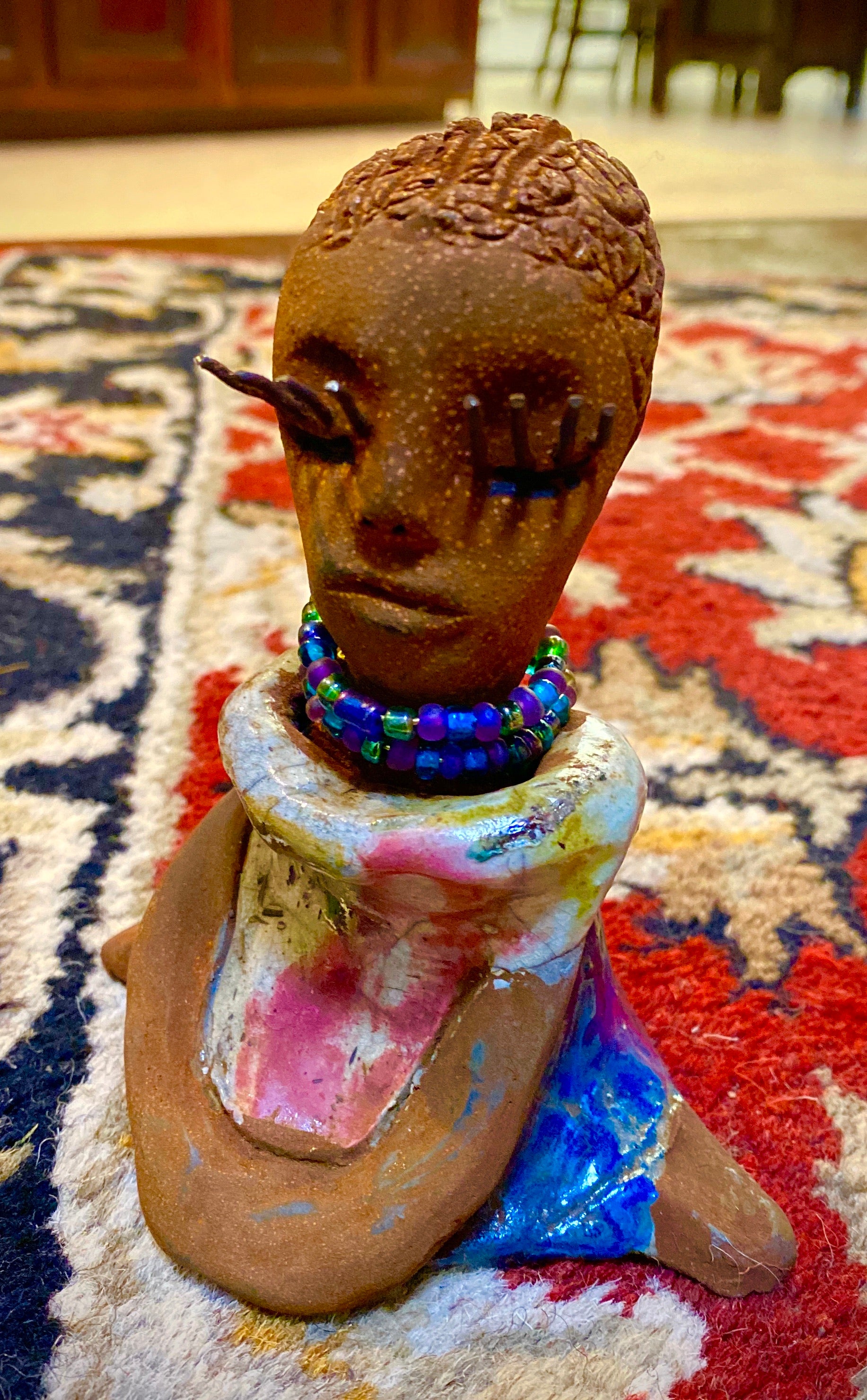 Riley stands 5" x 5”x 3" and weighs  11 ozs.  Riley has a lovely multicolored glossy dress with a matching beaded necklace.  She has long lashes!  Riley appears to sit in a yoga pose. Her long arms rest at her side.