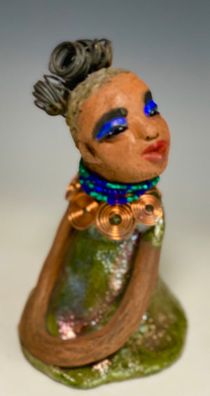 Meet Nia! Nia stands 8" x 6" x 6" and weighs 1.08 lbs. She has a lovely honey brown complexion with  reddish brown lips. She has a braided  wire bun hairstyle.  Nia has a colorful metallic green antique copper glazed dress. She wears a spiral copper wire necklaces with green beads underneath.  With eyes wide opened, Nia has hopes of finding her way into your home.