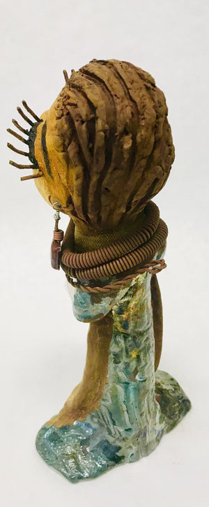Catera stands 10" x 4" x 4" and weighs 2.7 lbs. She has a lovely honey brown complexion with  reddish brown lips. She has a braided hairstyle.  Catera has a colorful metallic green antique copper glazed dress. She wears a yellow bead necklace with raku beads. Her long loving arms are resting at her side. With long lashes and eyes wide opened, Catera has hopes of finding a new home.