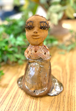 Charlotte stands 7" x 5" x 4" and weighs 1.03 lbs. She has a lovely honey brown complexion with  reddish brown lips. She has a braided hairstyle.  Charlotte has a colorful metallic  yellow green antique copper glazed dress. She wears a spiral copper wire necklace. With eyes slightly opened, Charlotte has hopes of finding a new home.   