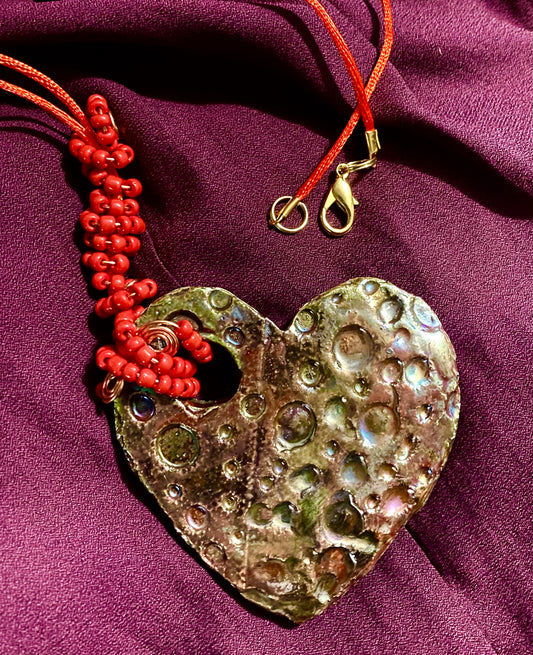  Have A Heart ! Each heart pendant is handmade with love! It is 3"x 3" and weighs approx. 3ozs. This pendant has a toasty copper metallic raku glazes that renders a unique translucent  patina. The heart has a textured pattern . Both sides are  are different and equally beautiful! It holds a spiral of red violet mini beads on a spiral copper wire. This pendant has a nice 12" red suede cord!