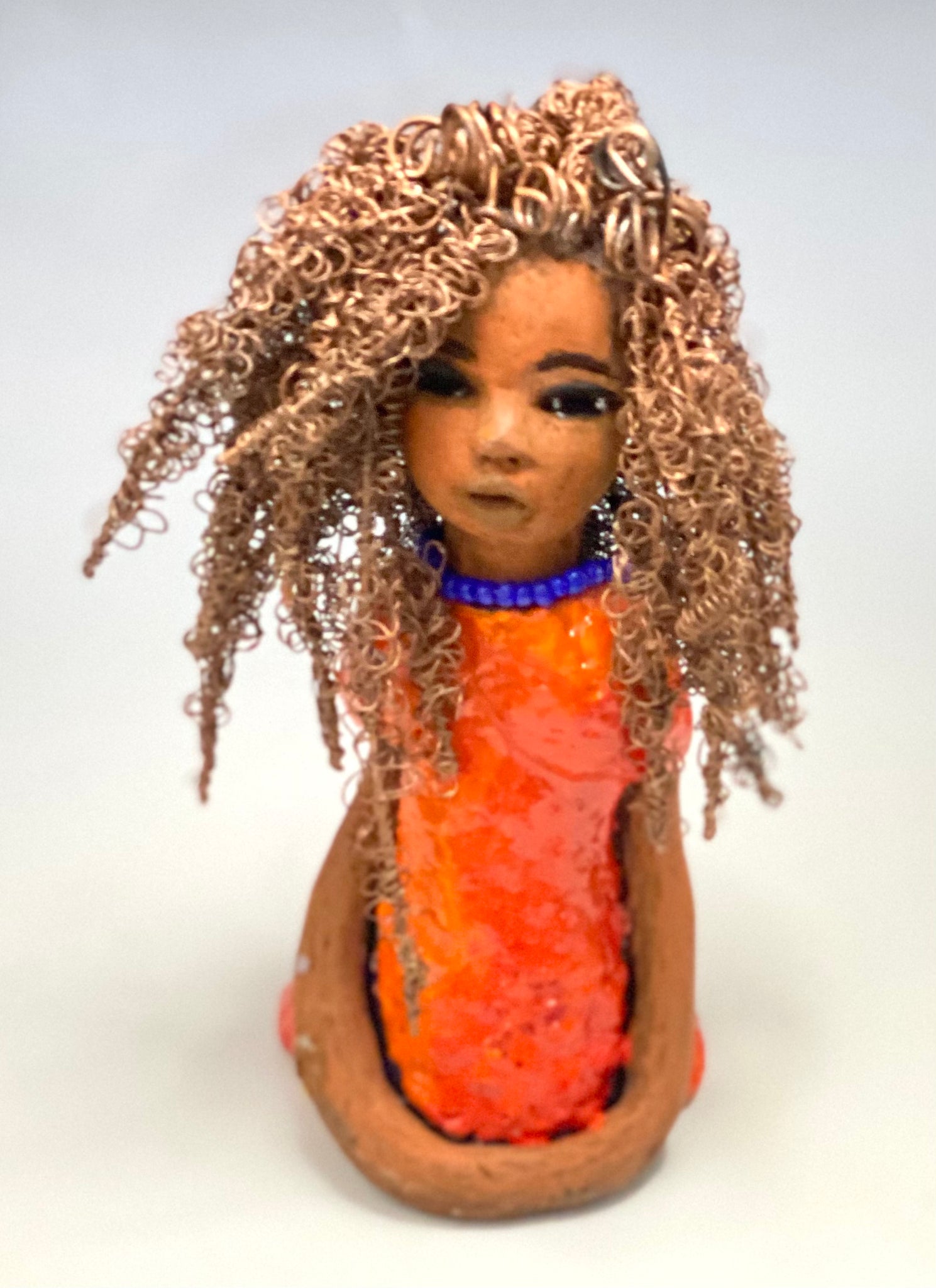 Meet Jada! Jada stands 8" x 3.5" x 3.5" and weighs 1 lb. She has a lovely honey brown complexion. Jada's dress is simply bright orange. She has her long loving arms resting at her side. " I am really pleased with Jada's blue beaded necklace and her new wire hair Find a place in your space for Jada!