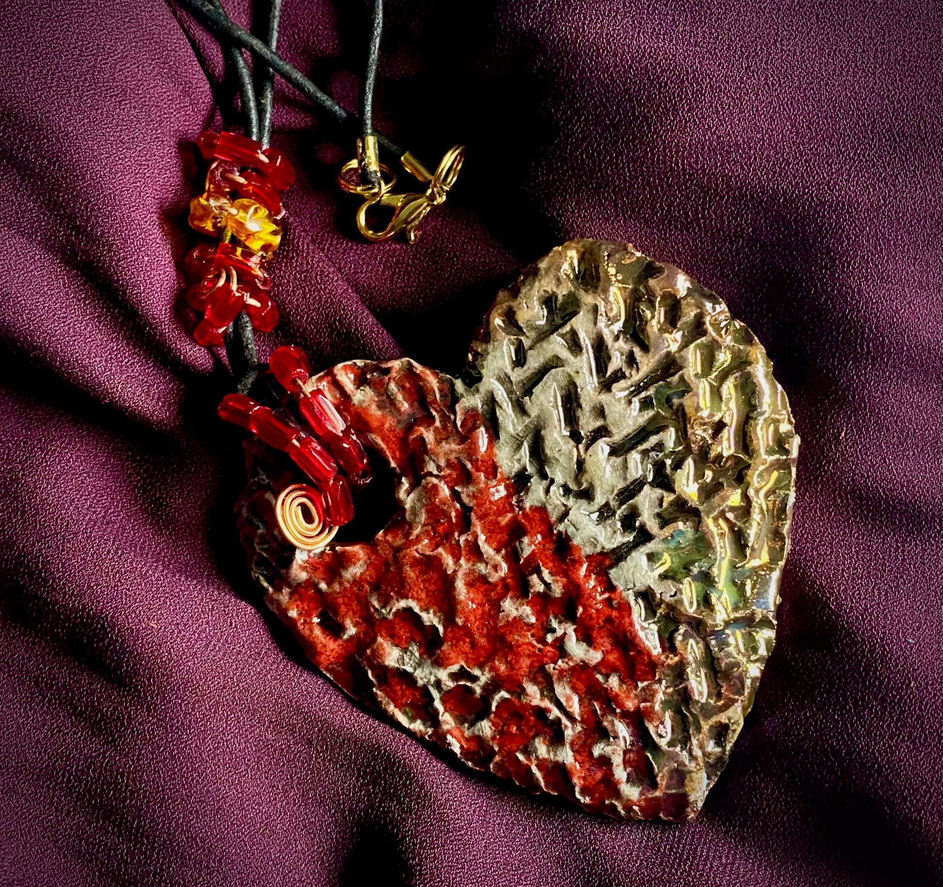 Have A Heart ! Each heart pendant is handmade with love! It is 3"x 3" and weighs approx. 3ozs. This pendant has a  ruby red and off white metallic raku glazes that renders a unique translucent  patina. The heart  has a textured  pattern. It holds a spiral of ruby red mini beads on a spiral copper wire. This pendant has a nice 12" black suede cord!