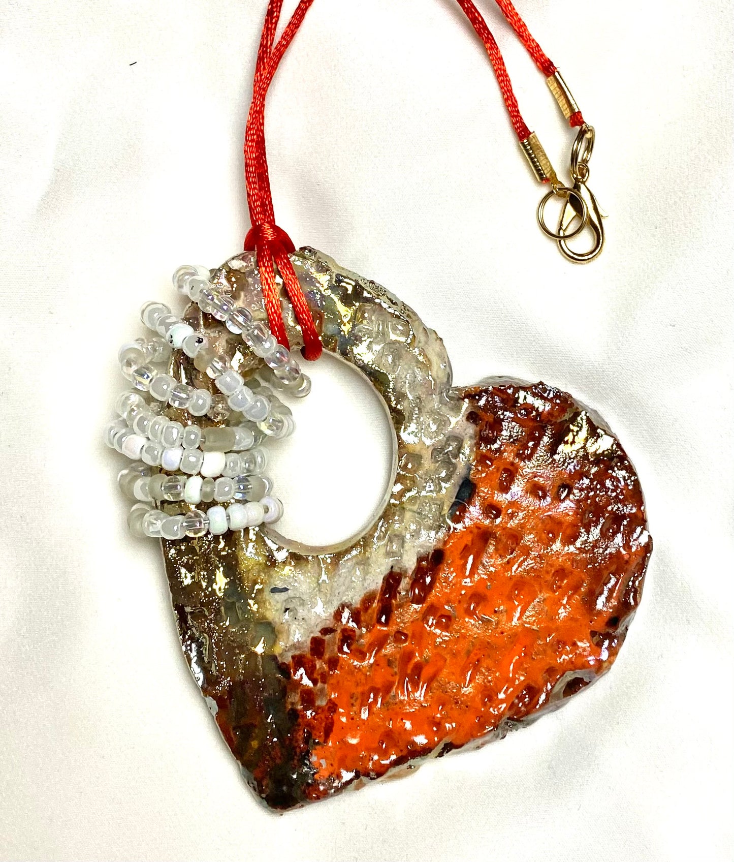 Have A Heart ! Each heart pendant is handmade with love! It is 3"x 3"and weighs approx. 3ozs. This pendant has a red violet and gold metallic raku glazes that renders a unique translucent  patina. The heart has a textured pattern . Both sides are  are different and equally beautiful! It holds a spiral of white and clear mini beads on a spiral copper wire. This pendant has a nice 12" red suede cord!