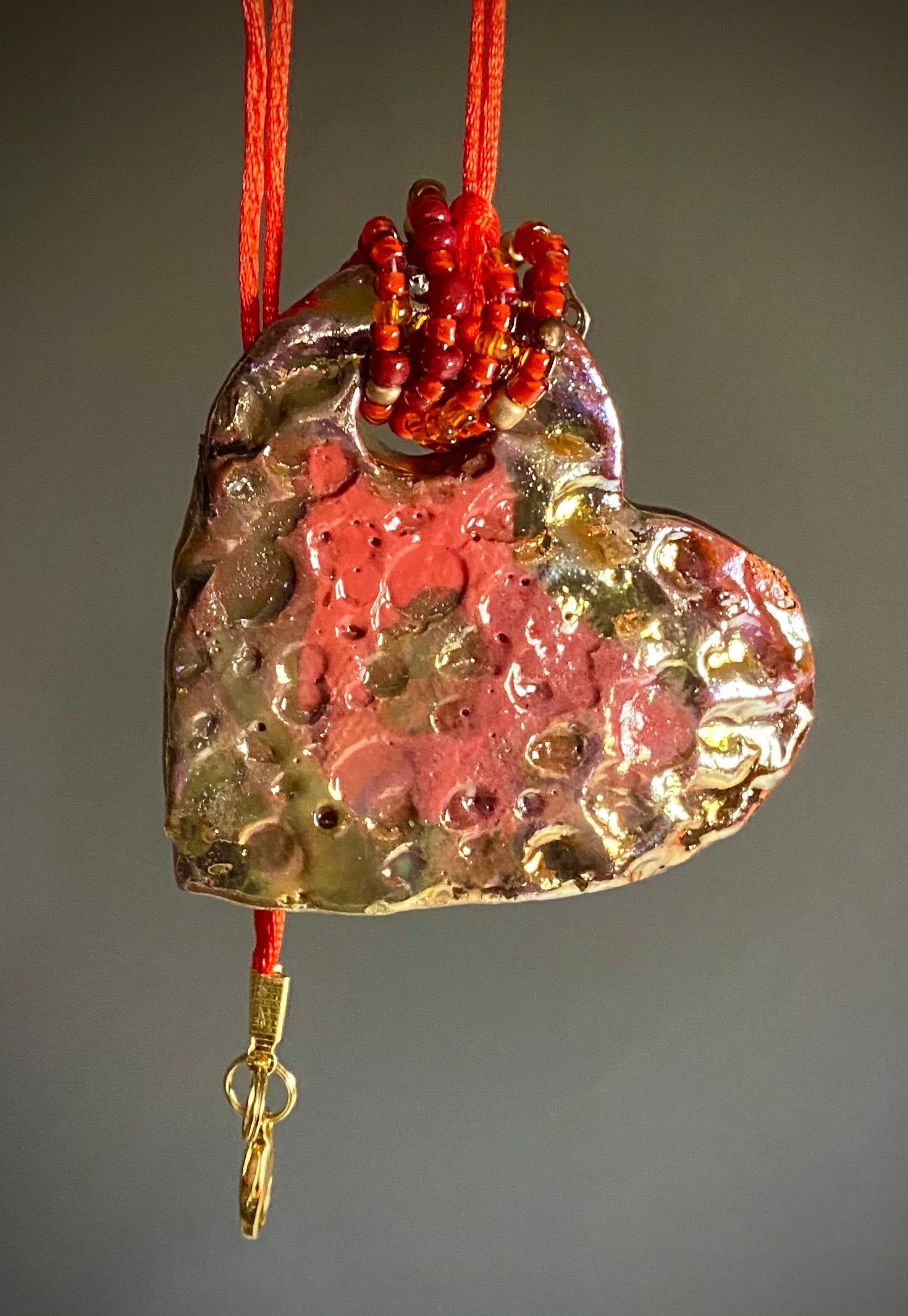 Have A Heart ! Each heart pendant is handmade with love! It is 3"x 3" and weighs approx. 3ozs. This pendant has a red violet and gold metallic raku glazes that renders a unique translucent  patina. The heart has a textured pattern . Both sides are  are different and equally beautiful! It holds a spiral of red violet mini beads on a spiral copper wire. This pendant has a nice 12" red suede cord!