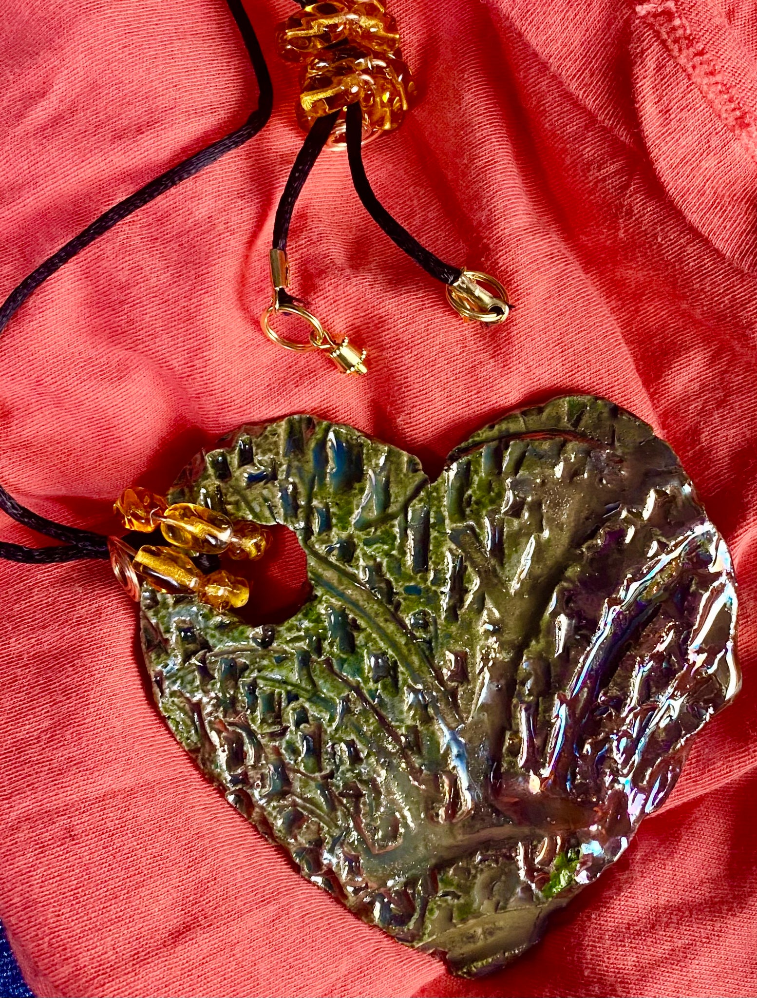 Have A Heart ! Each heart pendant is handmade with love! It is 3"x 3" and weighs approx. 3ozs. This pendant has an alligator green and gold metallic raku glazes that renders a unique translucent  patina. The heart  has a textured  pattern. It holds a spiral of amber mini beads on a spiral copper wire. This pendant has a nice 12" black suede cord!