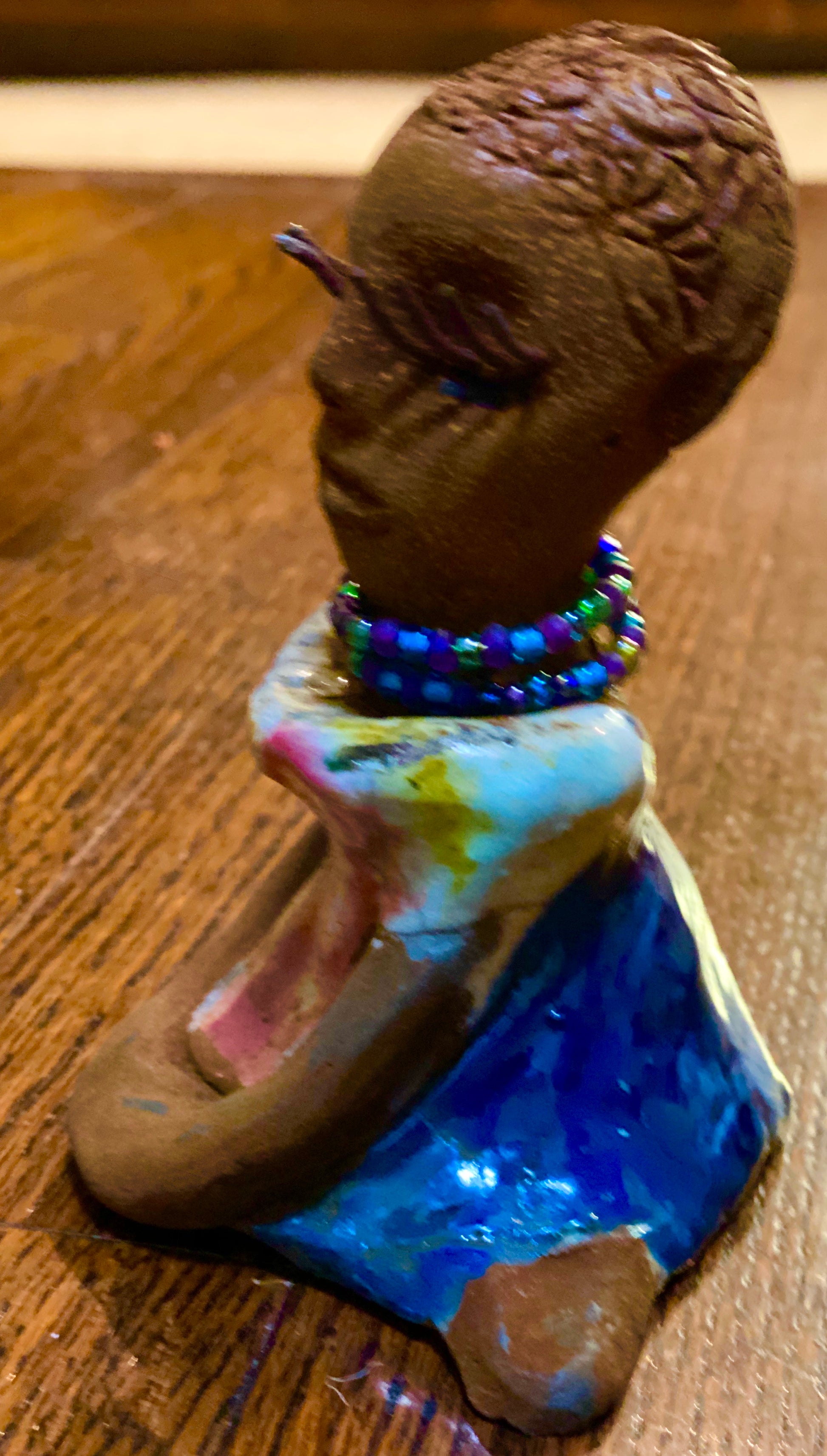Riley stands 5" x 5”x 3" and weighs  11 ozs.  Riley has a lovely multicolored glossy dress with a matching beaded necklace.  She has long lashes!  Riley appears to sit in a yoga pose. Her long arms rest at her side.