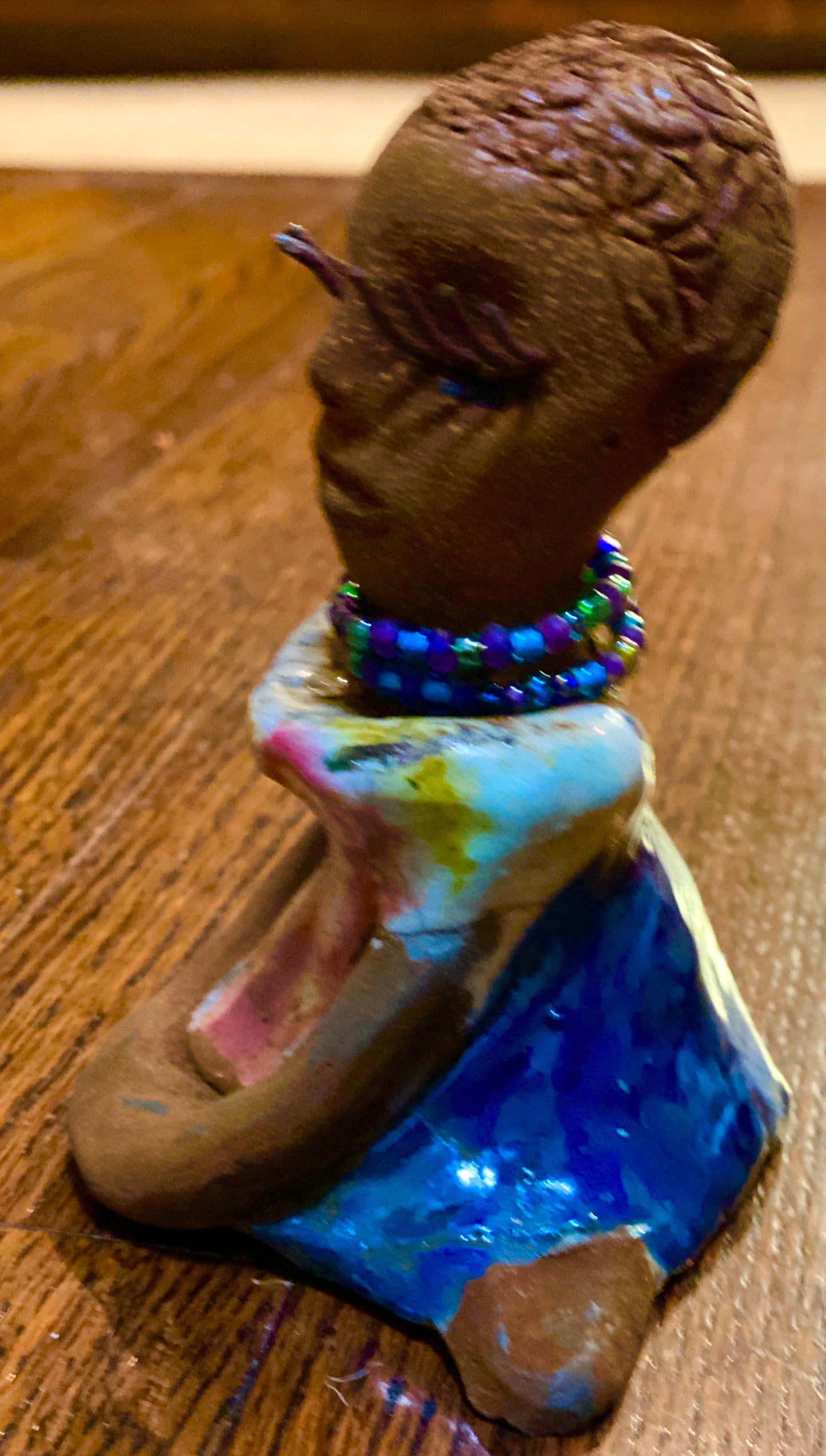 Riley stands 5" x 5”x 3" and weighs  11 ozs.  Riley has a lovely multicolored glossy dress with a matching beaded necklace.  She has long lashes!  Riley appears to sit in a yoga pose. Her long arms rest at her side.