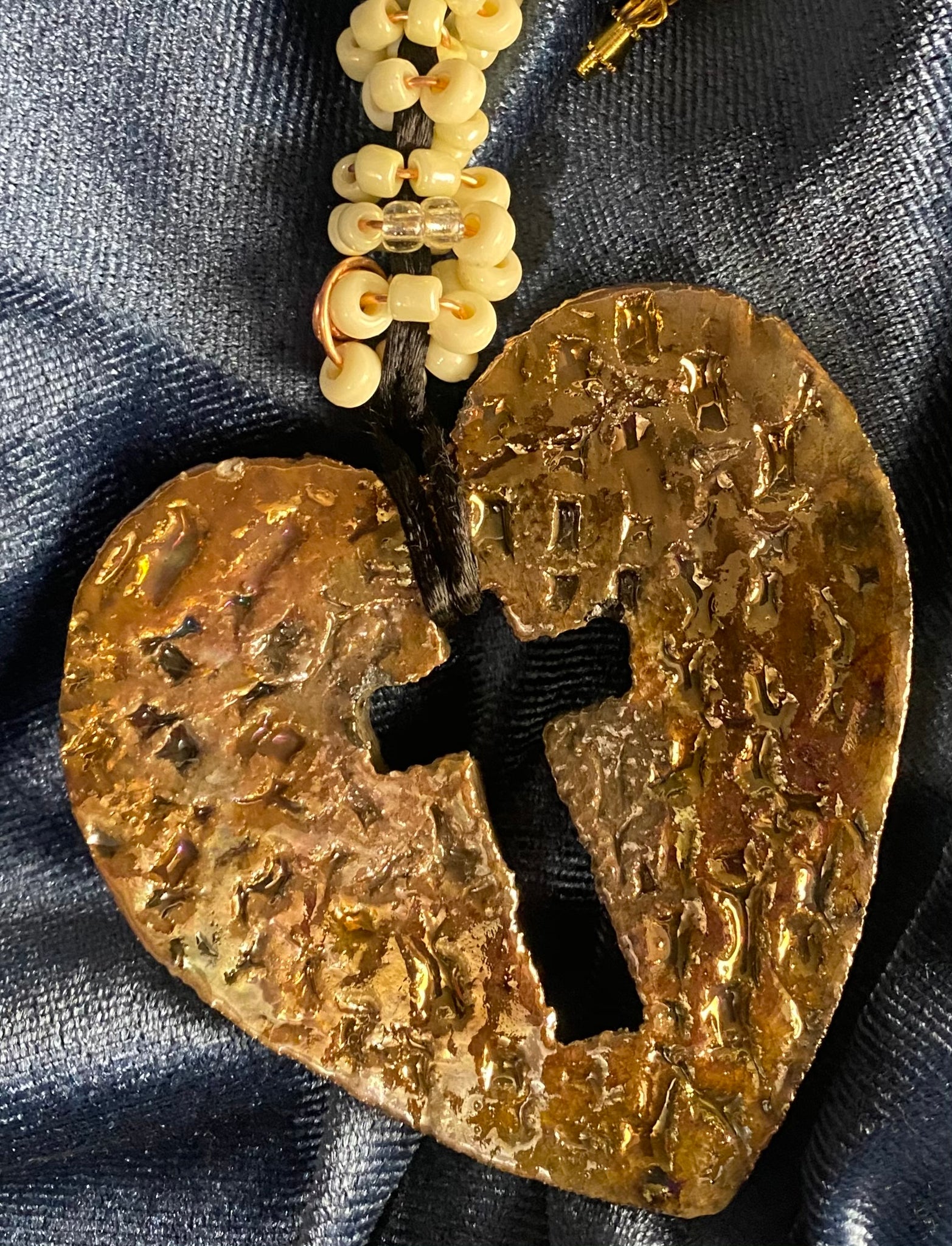 Have A Heart ! Each heart pendant is handmade with love! It is 3"x 3" and weighs approx. 3ozs. This pendant has an off white and gold metallic raku glazes that renders a unique translucent  patina. The heart  has a textured  pattern with a cut out cross in the center.. It holds a spiral of off white mini beads on a spiral copper wire. This pendant has a nice 12" black suede cord!