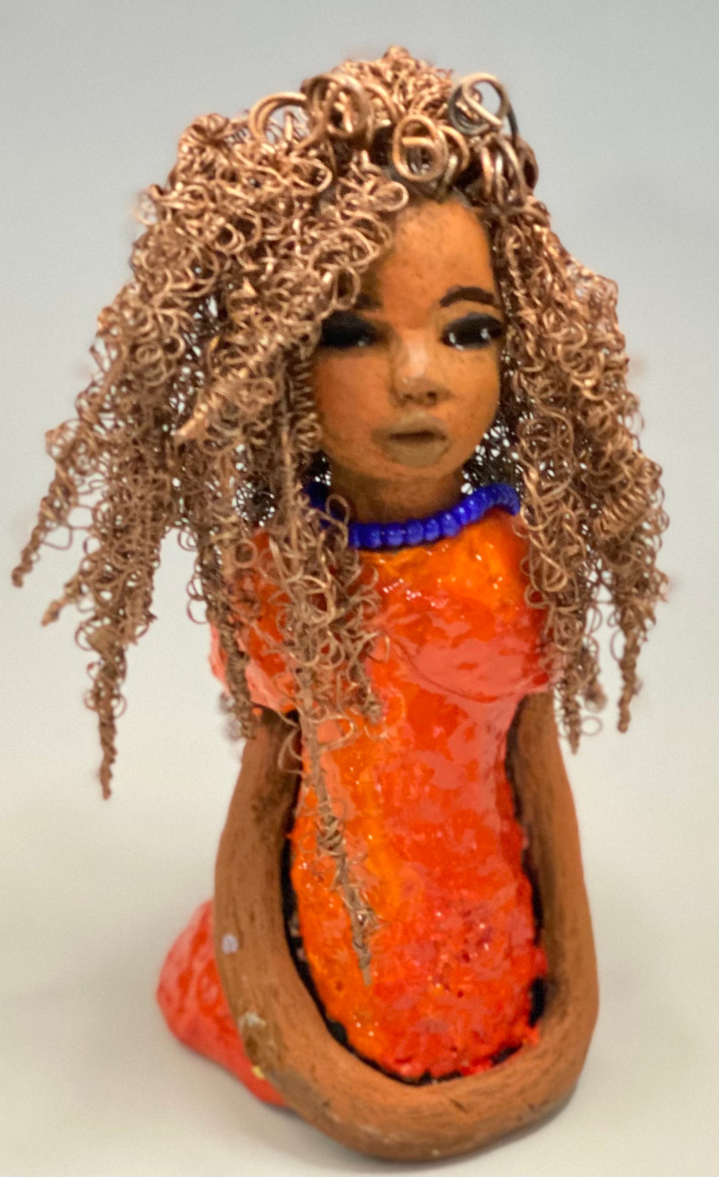 Meet Jada! Jada stands 8" x 3.5" x 3.5" and weighs 1 lb. She has a lovely honey brown complexion. Jada's dress is simply bright orange. She has her long loving arms resting at her side. " I am really pleased with Jada's blue beaded necklace and her new wire hair Find a place in your space for Jada!