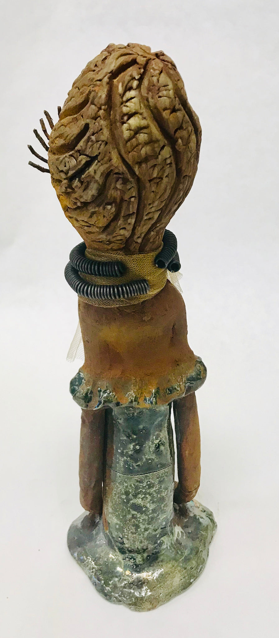 Trinity stands 14" x 4" x 4" and weighs 2.7 lbs. She has a lovely honey brown complexion with  reddish brown lips. She has a braided hairstyle.  Trinity has a colorful metallic green antique copper glazed dress. She wears a spiral wire necklaces with raku beads underneath an antique gold tulle.. With long lashes and eyes wide opened, Trinity has hopes of finding a new home.  
