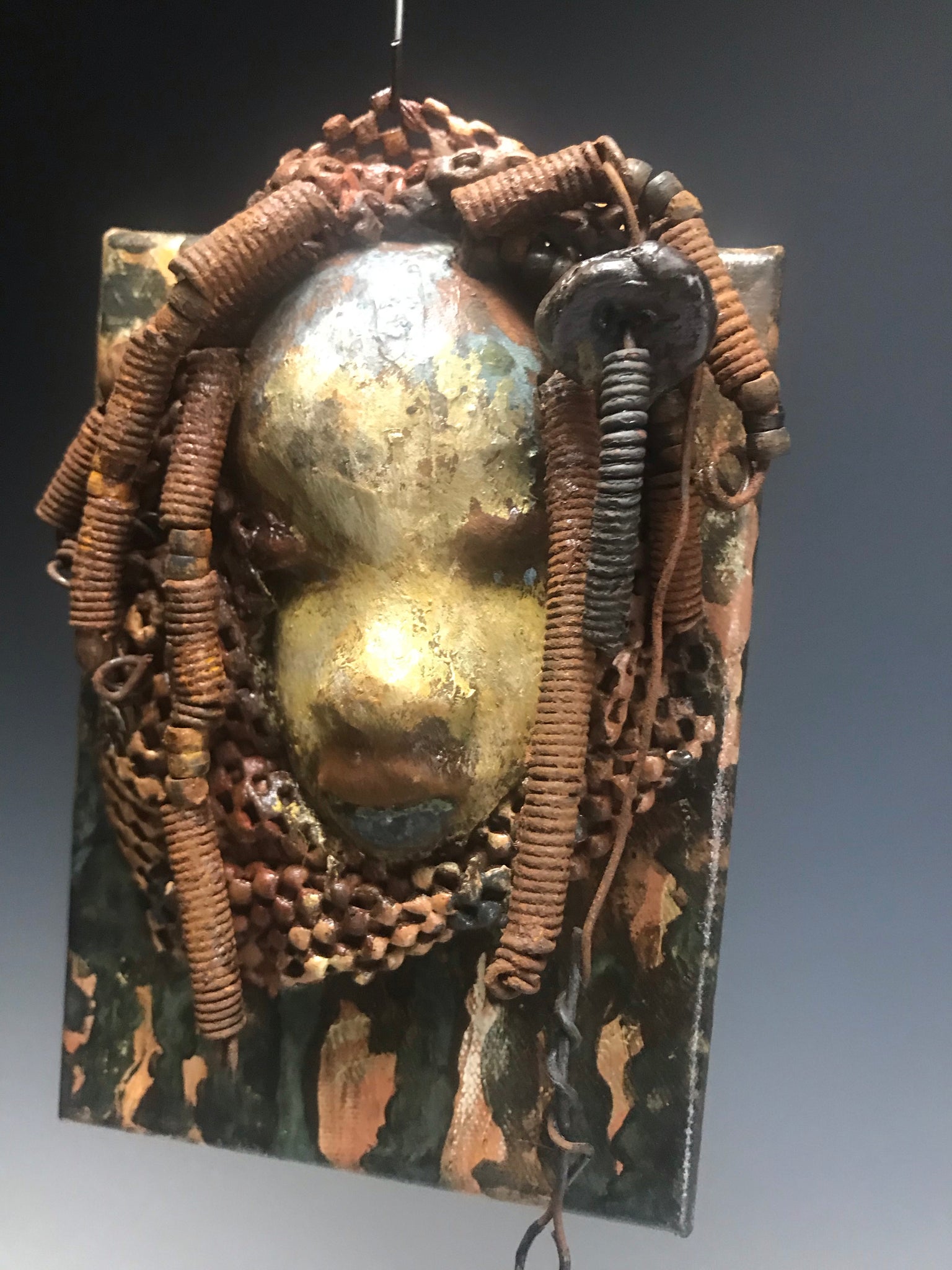"I started making mask after seeing an authentic African Mask collection at the Smithsonian Museum of African Art. I was in total awe. Dillan was inspired by my visit there".       Dillan is mounted on a painted 6"x 4"x 2" canvas. She weighs 15 ounces.     Her face is formed with hand coiled wire, multiple raku, and wood beads, matte textured  and brown cloth.     Dillan's face beams with  almond  green glaze and rust blue brown lips.     Dillan is ready to be hung.
