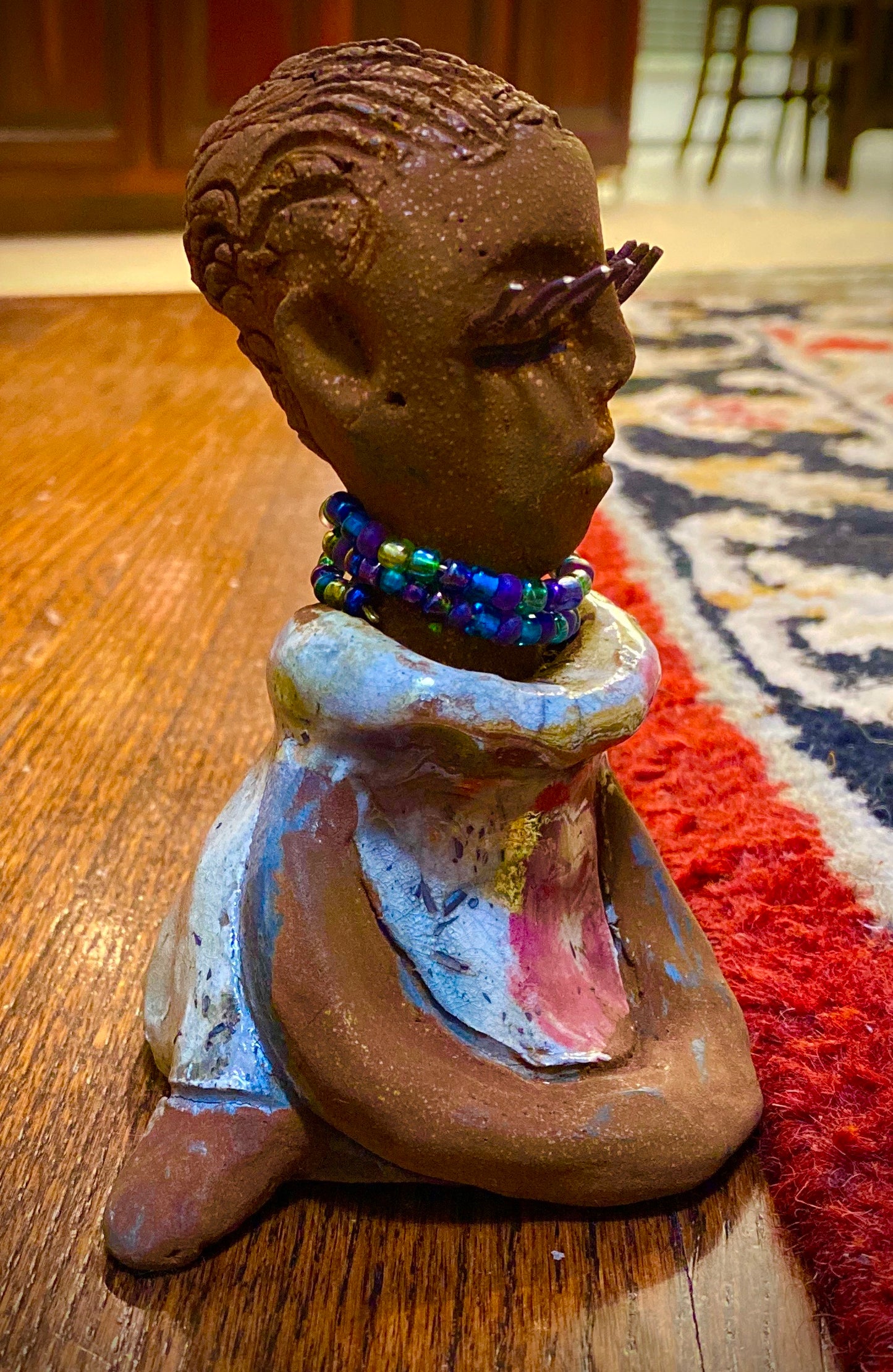 Riley stands 5" x 5”x 3" and weighs  11 ozs.  Riley has a lovely multicolored glossy dress with a matching beaded necklace.  She has long lashes!  Riley appears to sit in a yoga pose. Her long arms rest at her side.