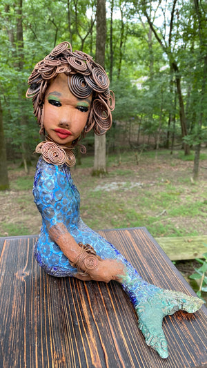Meet Shelia E.! She is such a Lady I mean Mermaid!    Shelia stands 12" x 10" x 4" and weighs 3.13 lbs. Shelia has a two tone honey brown complexion. She has over 15 feet of spiral wire hair which took over two hours to style. Shelia wears a textured sky blue swimsuit Her layered spiral copper necklace hangs above her long loving arm. Shelia is such a ladylike Mermaid. She sits tall and proud. Compare her to Harmony the mermaid. Give Shelia or Harmony a special place to sit in your home!