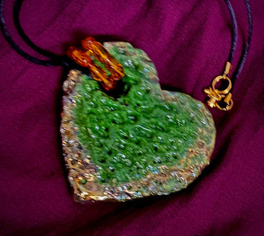 Have A Heart ! Each heart pendant is handmade with love! It is 3"x 3" and weighs approx. 3ozs. This pendant has a green and gold metallic raku glazes that renders a unique translucent  patina. The heart is highly textured. It holds a spiral of amber mini beads on a spiral copper wire. This pendant has a nice 12" black suede cord!