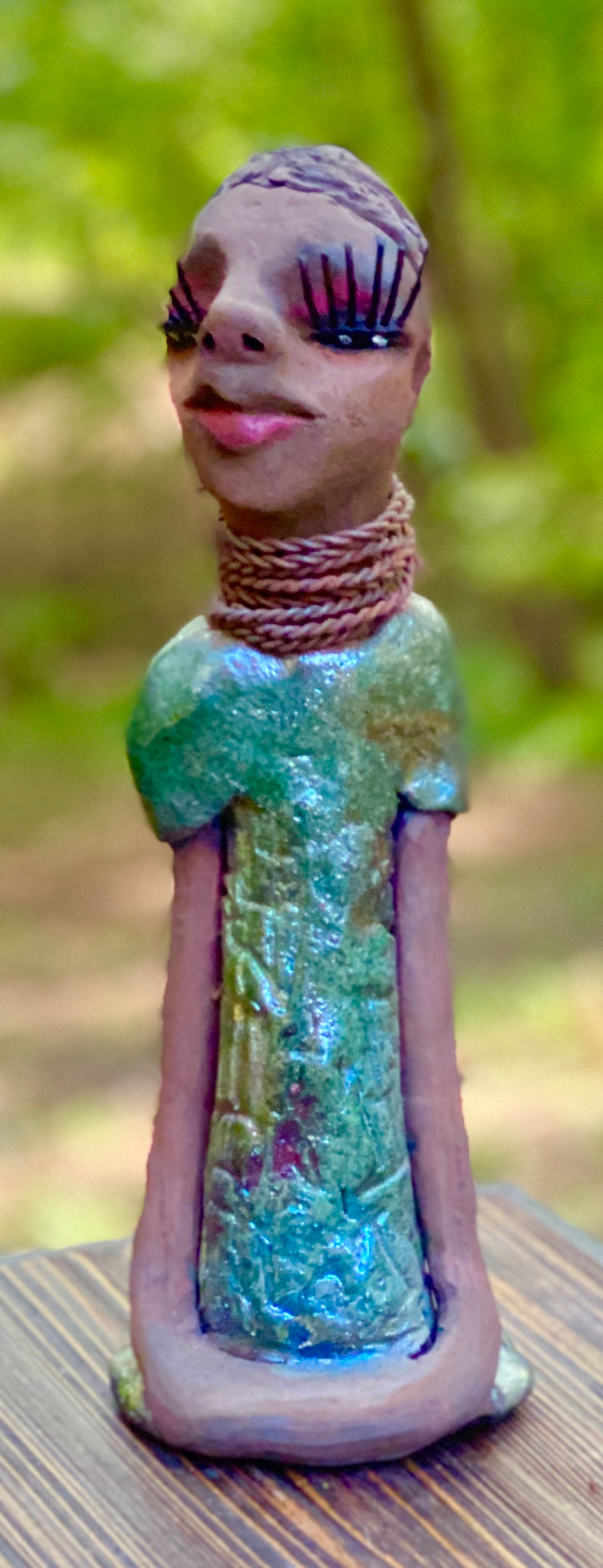Meet  Ingrid Ingrid stands 12" x 5" x 4" and weighs 1.14 lbs. She has a lovely honey brown complexion with  reddish brown lips. She has a braided hairstyle.  Ingrid has a colorful metallic green antique copper glazed dress. She wears six spiral wire necklaces.  Her long loving arms rest at her sides. With long lashes and eyes slightly opened, Ingrid has hopes of finding a new home!
