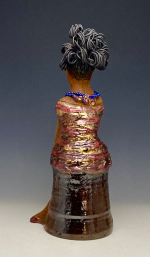 You know someone like Kim. One who reaps elegance and sophistication!  Kim stands 13" x 5" x 7" and weighs 2.07 lbs.  She has a lovely light beige complexion with over 4 feet of 16 gauge spiral coiled wire hair.  Kim's metallic copper red and gold dress is accented by a multicolored aqua blue beaded necklace. Kim's  maroon eye shadow gives her a distinguished mystical look. One must  wonder what is Kim thinking? Kim sits with her legs crossed as she awaits a special place to grace your home.