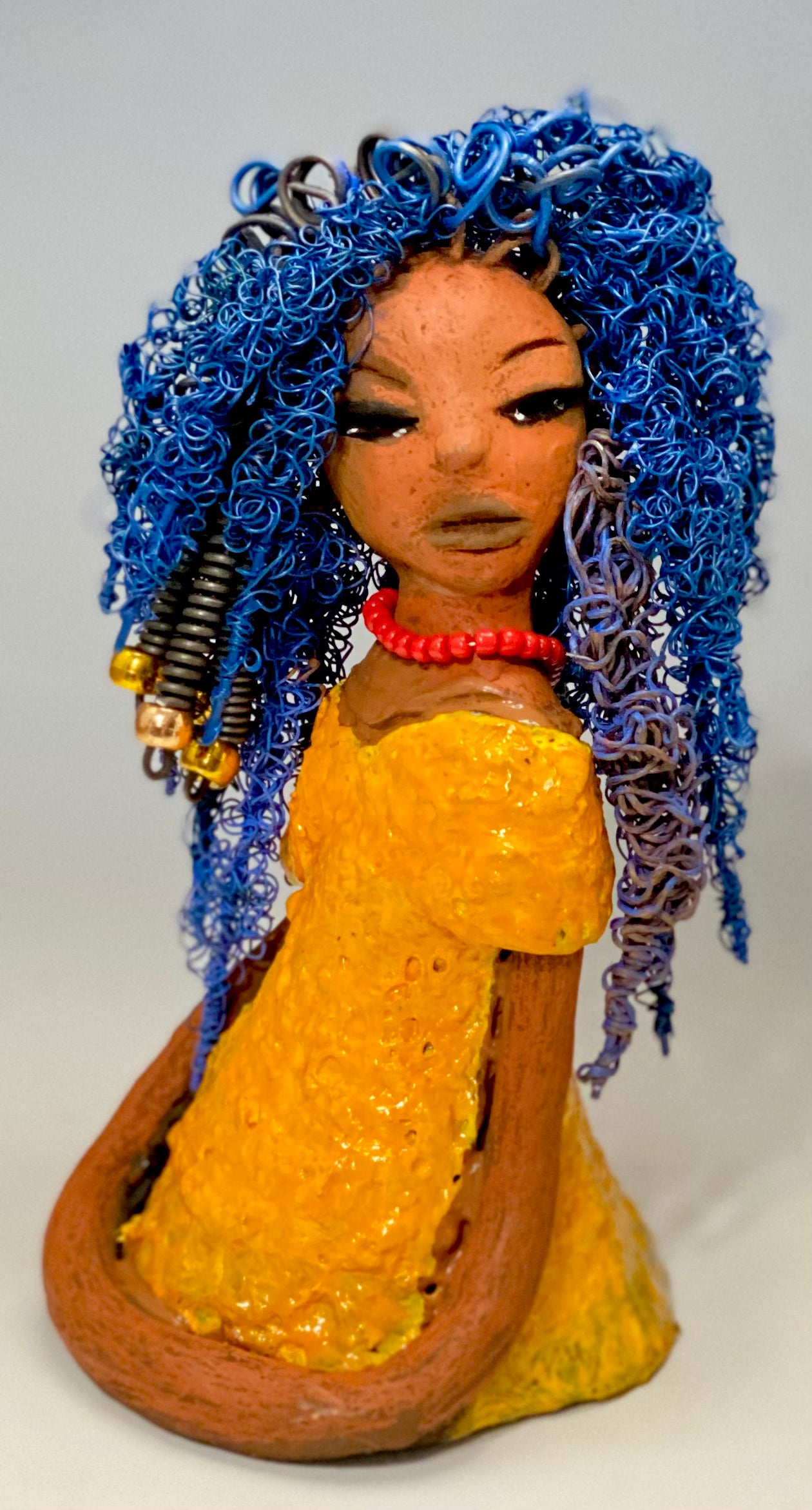 Makeba stands 8" x 5" x 5" and weighs 1.4 lbs. She has a lovely honey brown complexion with cocoa red lips. She has long twisted  blue wire locs hairstyle waist down!  Makeba has a sunset yellow red glazed dress. She has over 75 feet of 16 and 24 gauge blue wire for hair. It took over 5 hours just to do her hair! With  eyes wide opened and a subdue look, Makeba has hope of finding a new home.