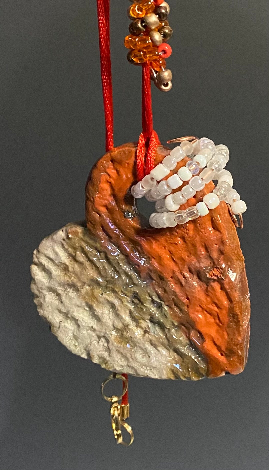 Have A Heart! Each heart pendant is handmade with love! It is 3"x 3"and weighs approx. 3ozs. This pendant has a  orange, white and gold metallic raku glazes that renders a unique translucent  patina. The heart has a textured pattern . Both sides are  are different and equally beautiful! It holds a spiral of white and orange  and amber mini beads on a spiral copper wire. This pendant has a nice 12" red adjustable rattail cord!