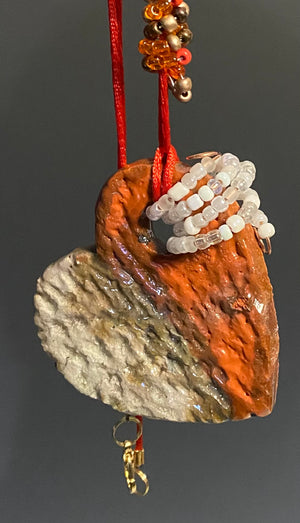 Have A Heart! Each heart pendant is handmade with love! It is 3"x 3"and weighs approx. 3ozs. This pendant has a  orange, white and gold metallic raku glazes that renders a unique translucent  patina. The heart has a textured pattern . Both sides are  are different and equally beautiful! It holds a spiral of white and orange  and amber mini beads on a spiral copper wire. This pendant has a nice 12" red adjustable rattail cord!
