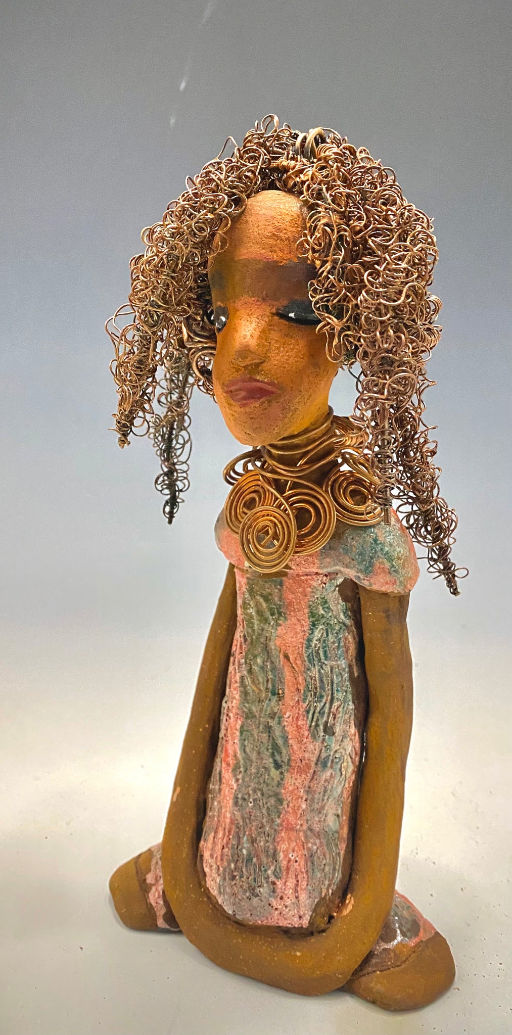 " I am really pleased with Jada's copper coiled necklace and her new wire hair. It complements her well!" Jada stands 9" x 4.5" x 2.5" and weighs 1 lb. She has a lovely two tone honey brown complexion. Jada's dress is a metallic glaze with copper red stripes. She has her long loving arms resting at her side. Find a place in your space for Jada!