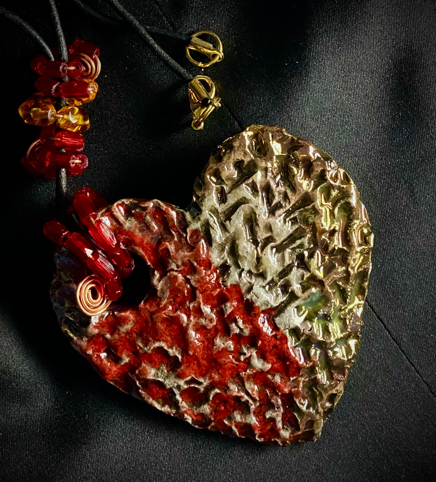 Have A Heart ! Each heart pendant is handmade with love! It is 3"x 3" and weighs approx. 3ozs. This pendant has a  ruby red and off white metallic raku glazes that renders a unique translucent  patina. The heart  has a textured  pattern. It holds a spiral of ruby red mini beads on a spiral copper wire. This pendant has a nice 12" black suede cord!