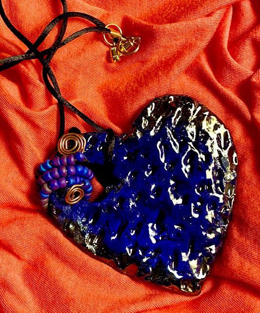 Have A Heart ! Each heart pendant is handmade with love! It is 3"x 3" and weighs approx. 3ozs. This pendant has a royal blue and gold metallic raku glazes that renders a unique translucent  patina. The heart  has a textured  pattern. It holds a spiral of off blue violet mini beads on a spiral copper wire. This pendant has a nice 12" black suede cord!