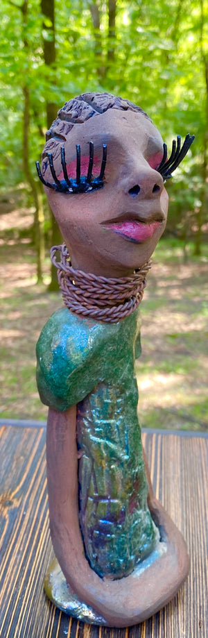 Meet  Ingrid Ingrid stands 12" x 5" x 4" and weighs 1.14 lbs. She has a lovely honey brown complexion with  reddish brown lips. She has a braided hairstyle.  Ingrid has a colorful metallic green antique copper glazed dress. She wears six spiral wire necklaces.  Her long loving arms rest at her sides. With long lashes and eyes slightly opened, Ingrid has hopes of finding a new home!