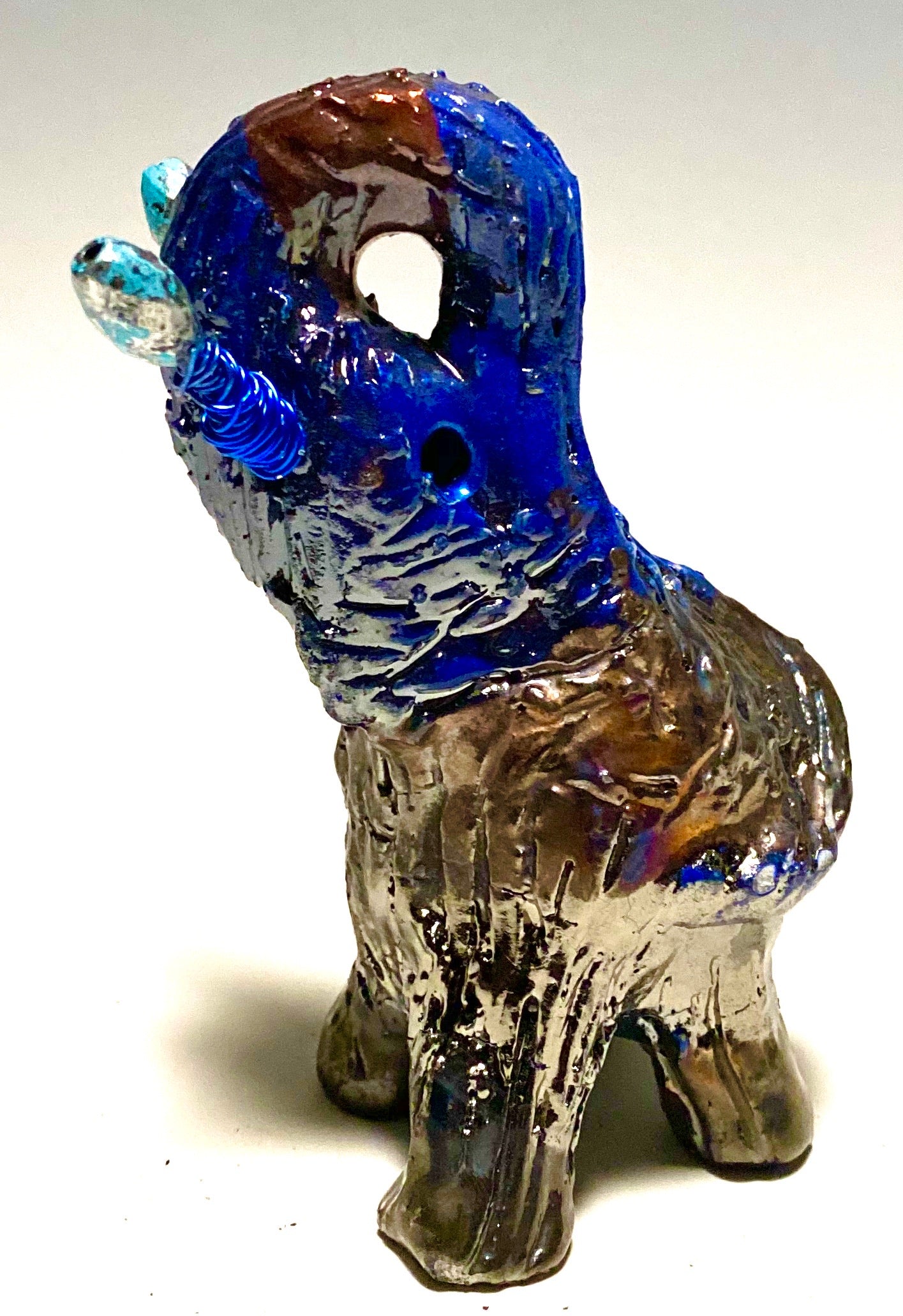 Raku Elephant Have you HERD!!!!!!  Just one of these lovely Raku Fired Elephant will make an excellent gift for your  friend, sorority or for your home’ special place centerpiece.  5" x 4" x 4" 9 ozs. Blue wire beaded blue tusk Beautiful metallic raku colors For decorative purposely only.