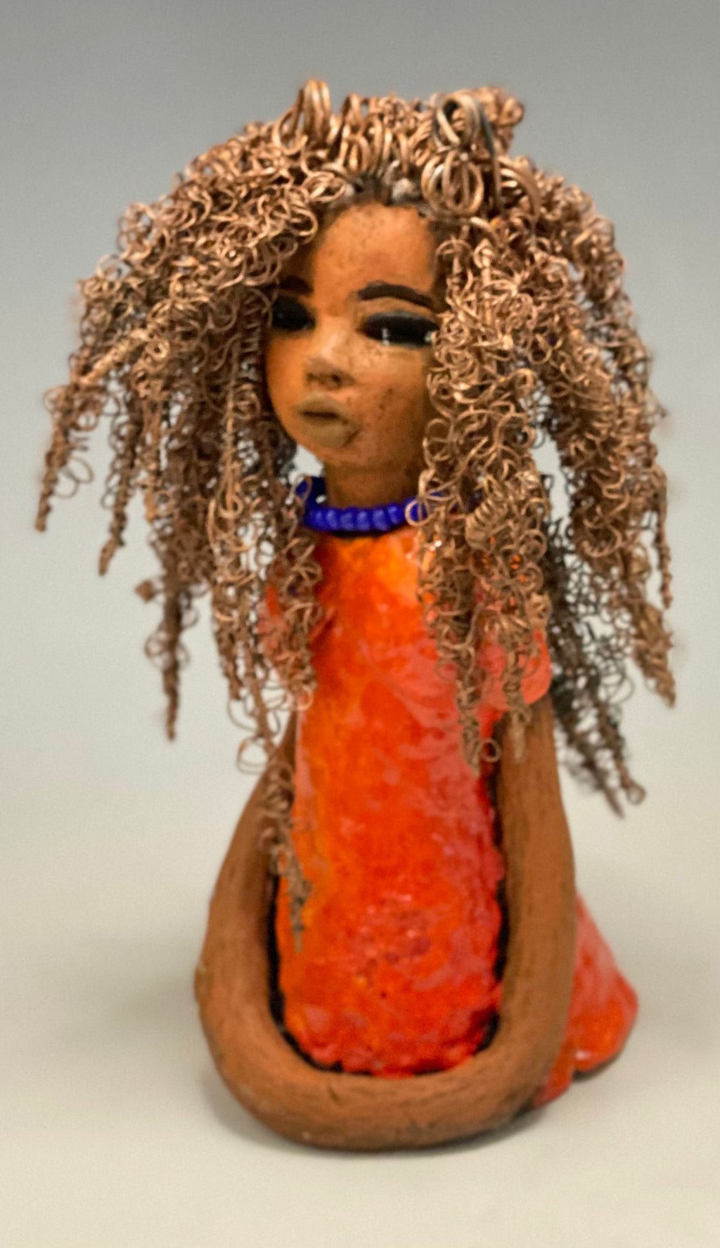 Meet Jada! Jada stands 8" x 3.5" x 3.5" and weighs 1 lb. She has a lovely honey brown complexion. Jada's dress is simply bright orange. She has her long loving arms resting at her side. " I am really pleased with Jada's blue beaded necklace and her new wire hair Find a place in your space for Jada!