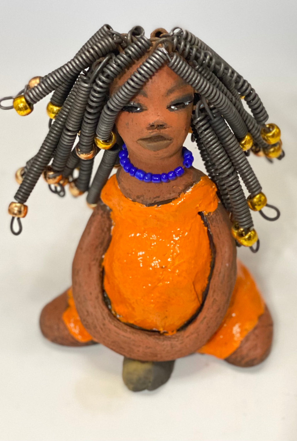  Meet Destiny!  Destiny stands 6.5" x 5" x 4" and weighs 1.05 lbs. She wears a lovely glossy sunset orange dress adorn by a blue beaded necklace. Destiny has over25 feet of 16 gauge coiled wire hair with gold beads.. Destiny appears to sit in a yoga pose. Her long arms rest at her side. Destiny is a great starter piece from the Herdew Collection!