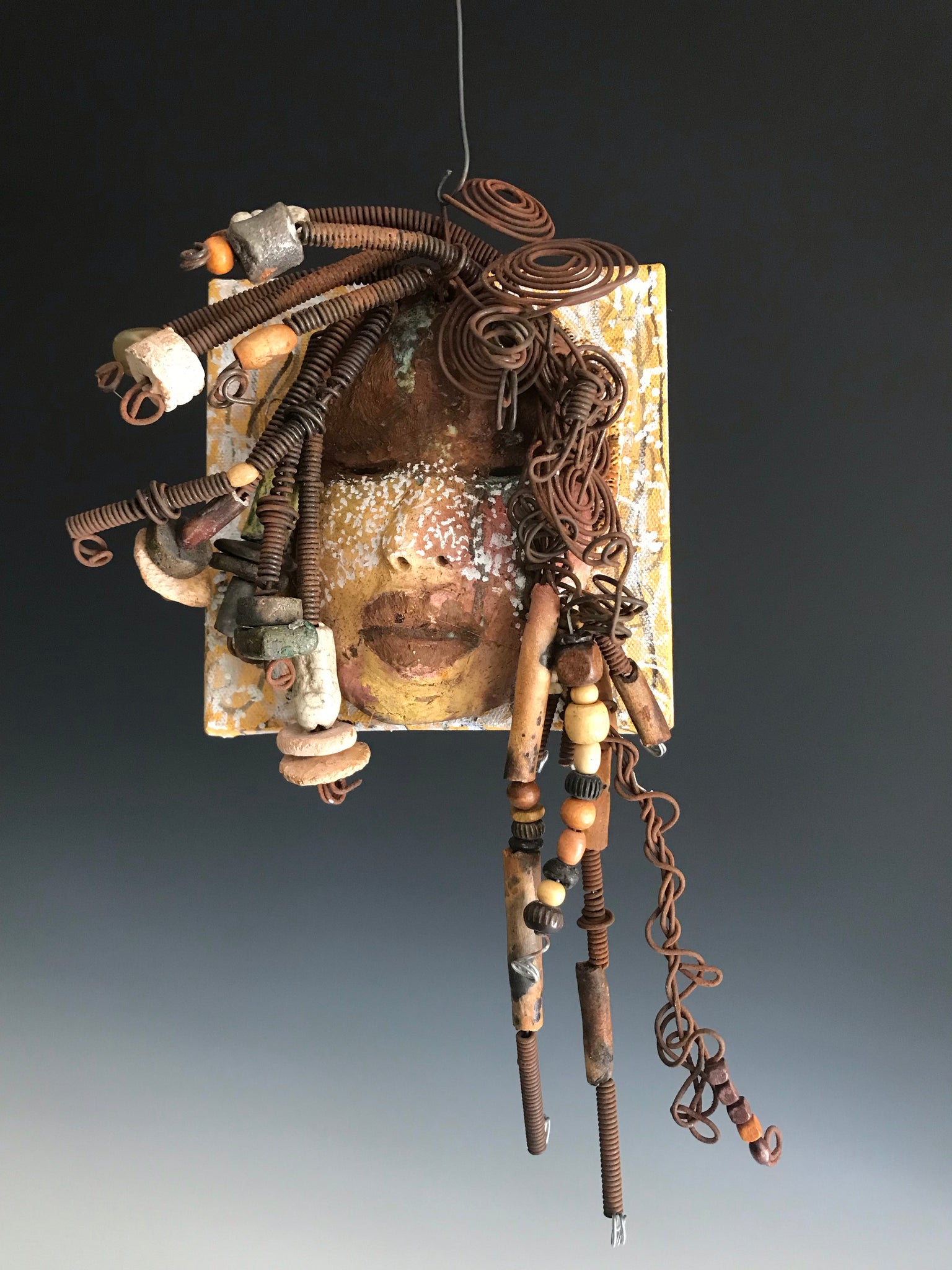     Iowa is uniquely mounted on a painted 6"x 4"x 2" canvas. It weighs 1.13 lbs.     Her face has white dots over an earthy.glaze with dark brown lips.     Iowa has  hand coiled wire, multi color raku beads,wood beads, and textured earthy cloth..  Iowa is ready to be hung!