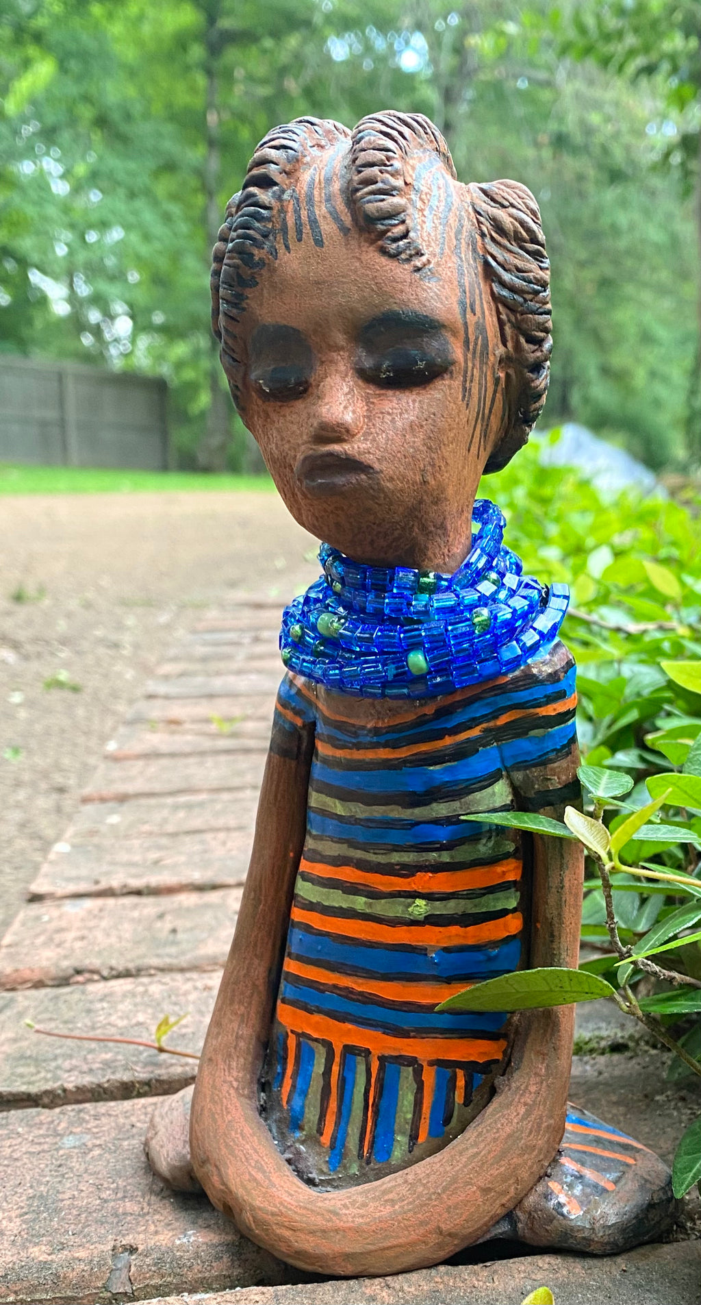 Meet Meet Harmony! Harmony stands 8' x 5"x 2" and weighs 1.7 lb. She has a nice honey brown complexion. Harmony  has stylized clay hair.  Her long trademark arms rest at her side. Harmony's dress is  colorful with  geometric flare.. She accents with a aqua blue beaded necklace. Harmony is priced right to be accepted into  your home! 