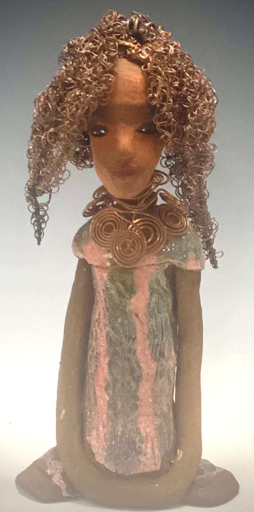 " I am really pleased with Jada's copper coiled necklace and her new wire hair. It complements her well!" Jada stands 9" x 4.5" x 2.5" and weighs 1 lb. She has a lovely two tone honey brown complexion. Jada's dress is a metallic glaze with copper red stripes. She has her long loving arms resting at her side. Find a place in your space for Jada!