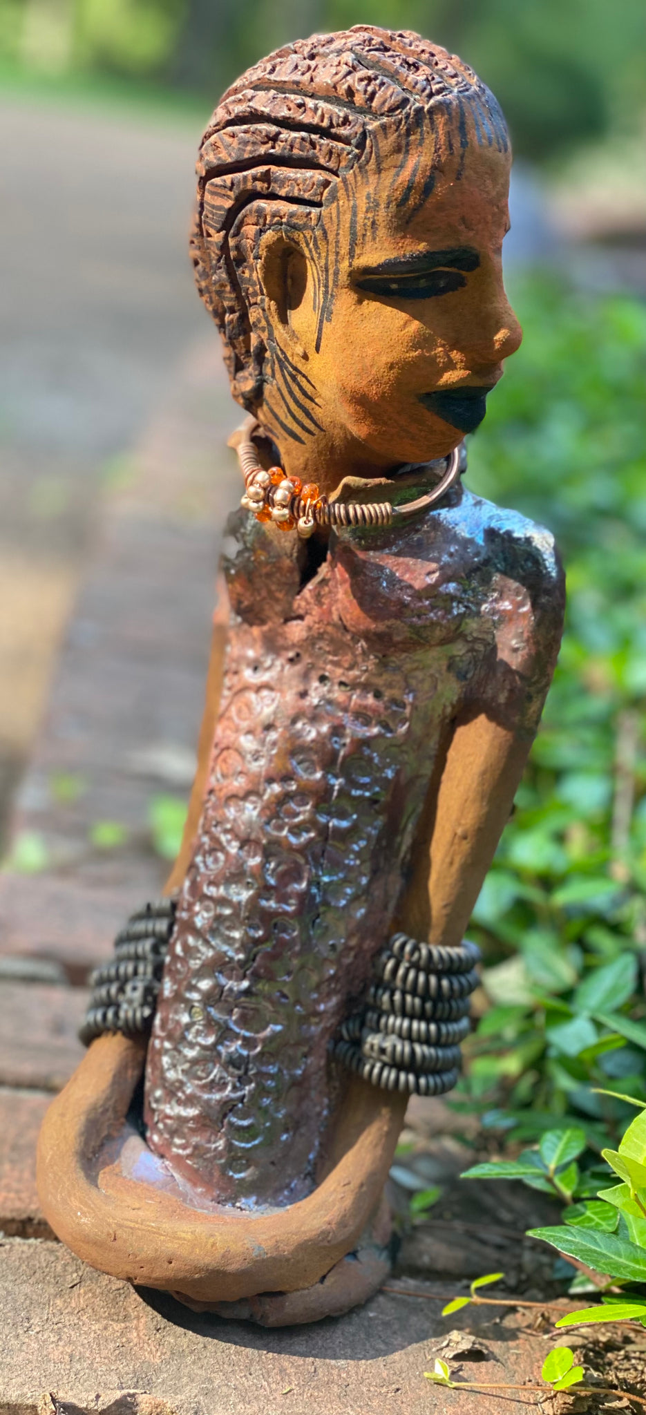 Jessie says no to wire hair and yes to the braids. Jessie stands 12" x 5" x 4.5" and weighs 1.03 lbs. She has a lovely honey brown complexion.  Jessie long loving arms rest beside her alligator copper green dress. She wears a strand of amber beads with spiral copper that can be worn as a bracelet. Jessie is a sophisticated lady that will grace your home.