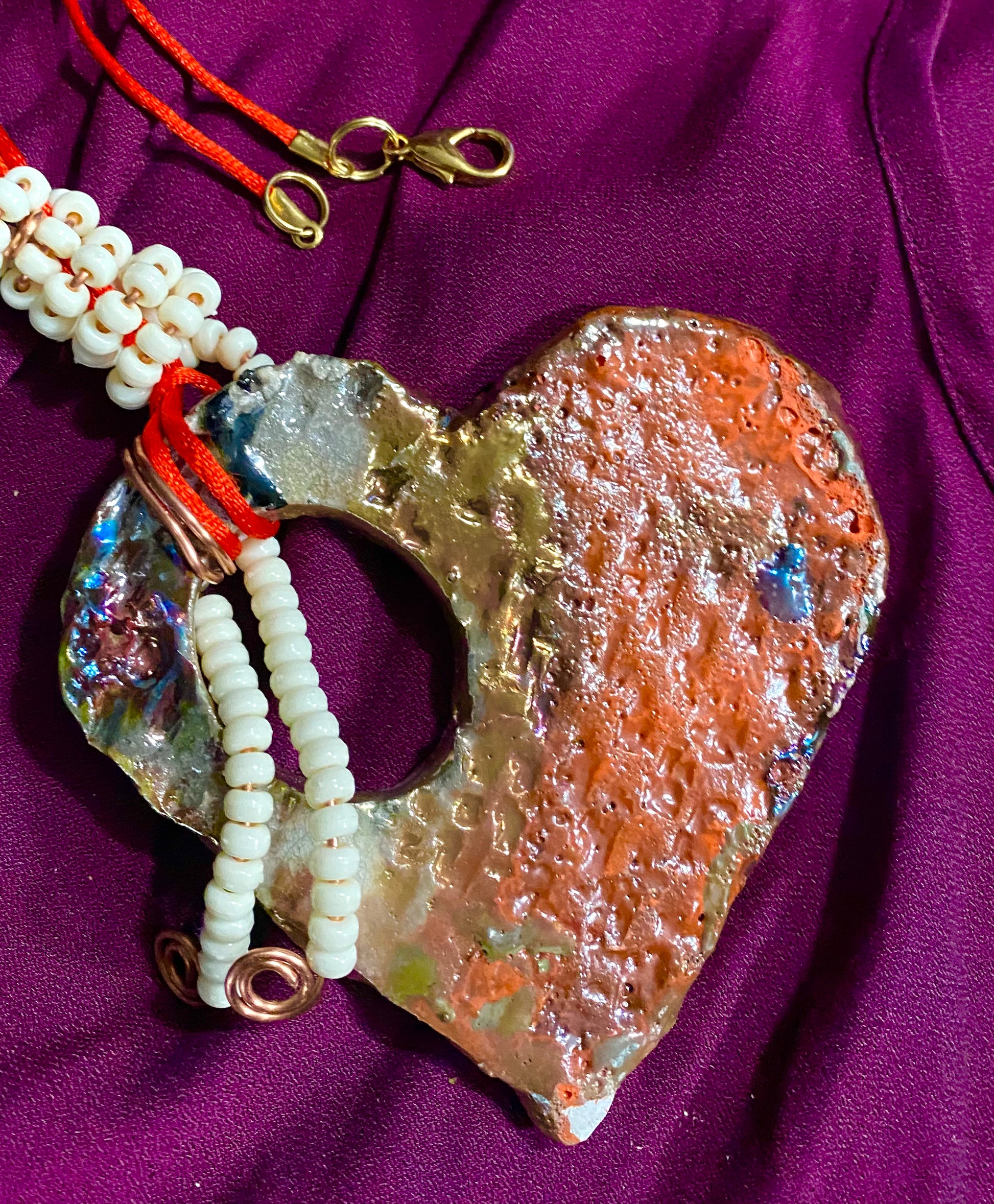 Have A Heart! Each heart pendant is handmade with love! It is 3"x 3"and weighs approx. 3ozs. This pendant has a red,orange, white and copper metallic raku glazes that renders a unique translucent  patina. The heart has a textured pattern . Both sides are  are different and equally beautiful! There is a spiral white mini beads on copper in the center. This pendant has a nice 12" red adjustable rattail cord!