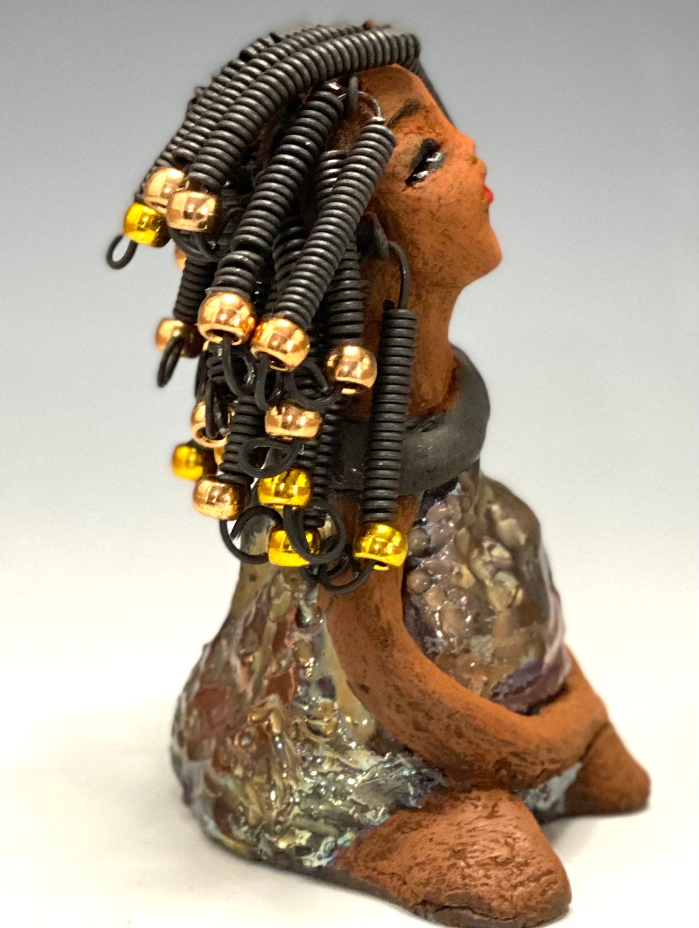   Meet Sadie  Sadie stands 5.5" x 4" x 3" and weighs 8.7 ozs. She wears a lovely glossy  metallic gold dress.. Sadie has over15 feet of coiled wire hair. Sadie appears to sit in a yoga pose. Her long arms rest at her side. Sadie is a great starter piece from the Herdew Collection!