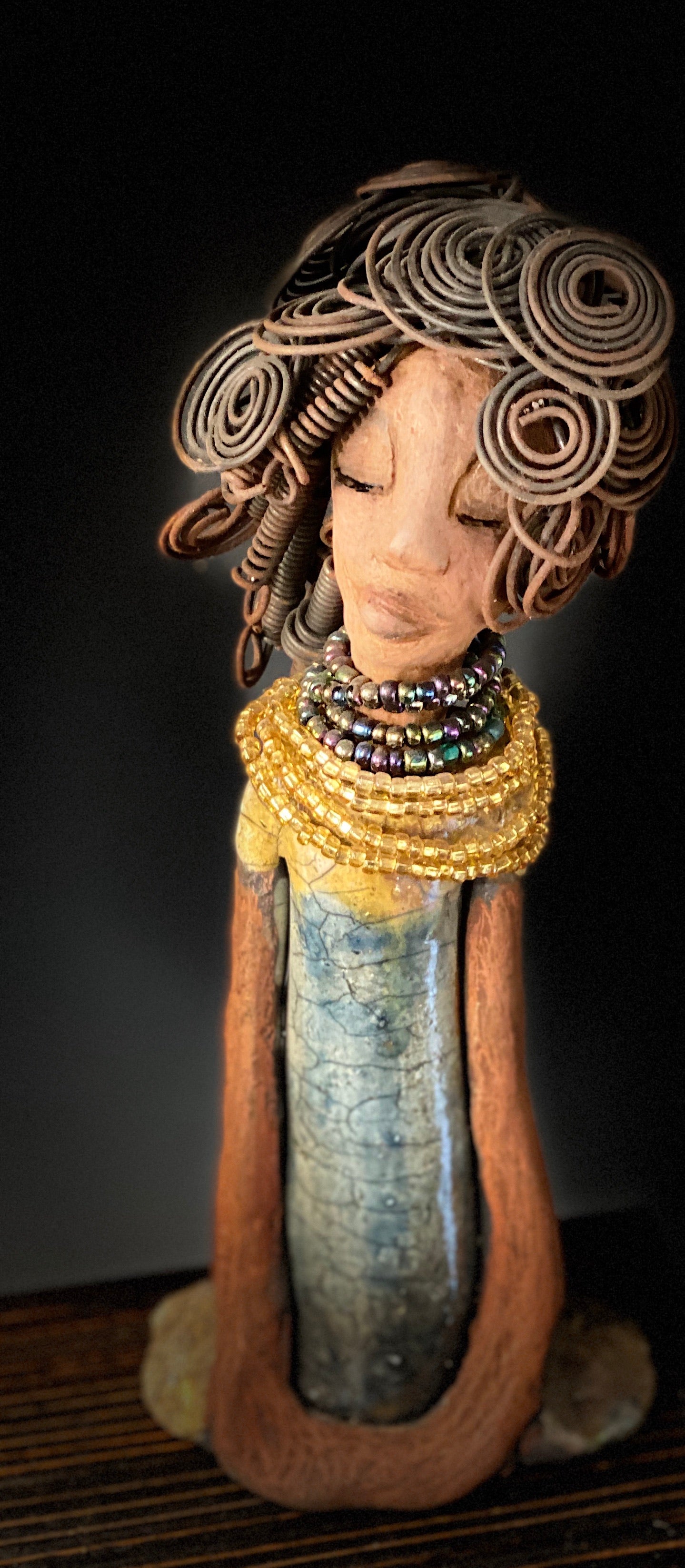 Sophia knows but will never tell! Sophia stands 10.5" x 4" x 3" and weighs 1.10 lbs. She has a  honey brown complexion with curls, coils and twisted, wire hair. Sophia wears a light blue crackle dress with a dazzling gold and multicolored beaded necklace. Yes, Sophia knows something but she will never tell. Sophia will spark a conversation of "say what" in your place.