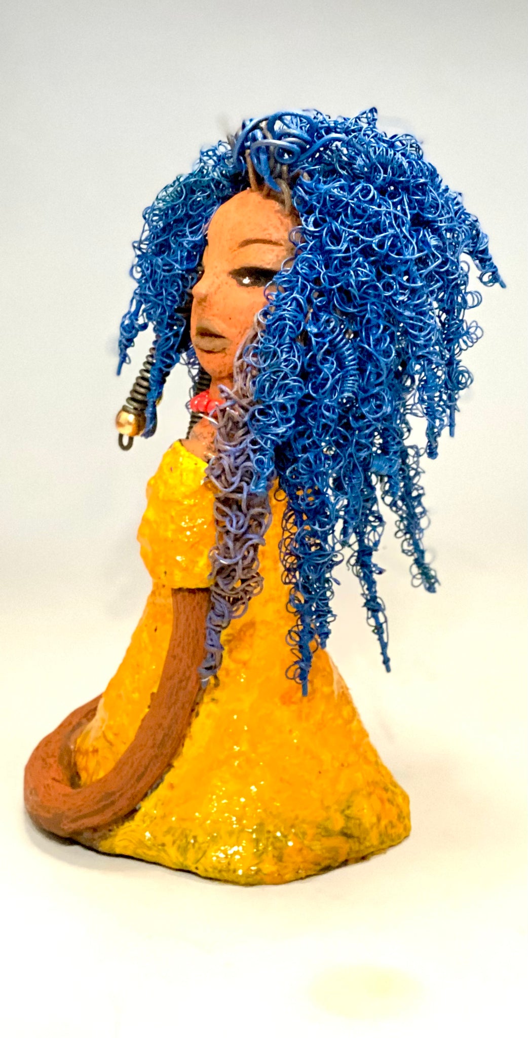 Makeba stands 8" x 5" x 5" and weighs 1.4 lbs. She has a lovely honey brown complexion with cocoa red lips. She has long twisted  blue wire locs hairstyle waist down!  Makeba has a sunset yellow red glazed dress. She has over 75 feet of 16 and 24 gauge blue wire for hair. It took over 5 hours just to do her hair! With  eyes wide opened and a subdue look, Makeba has hope of finding a new home.