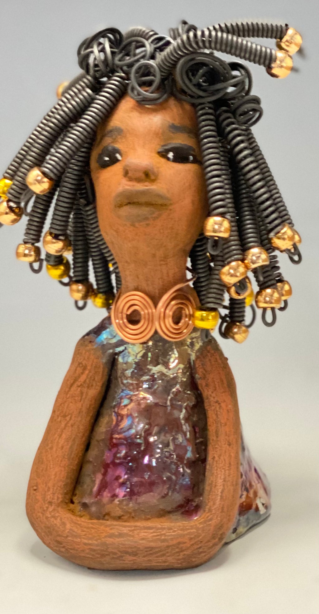   Meet Alexus  Alexus stands 7.5" x 4" x 4" and weighs 1.05 lbs. She wears a lovely glossy  metallic gold dress adorn by a spiral copper necklace. Alexus has over15 feet of coiled wire hair with gold beads.. Alexus appears to sit in a yoga pose. Her long arms rest at her side. Alexus is a great starter piece from the Herdew Collection!
