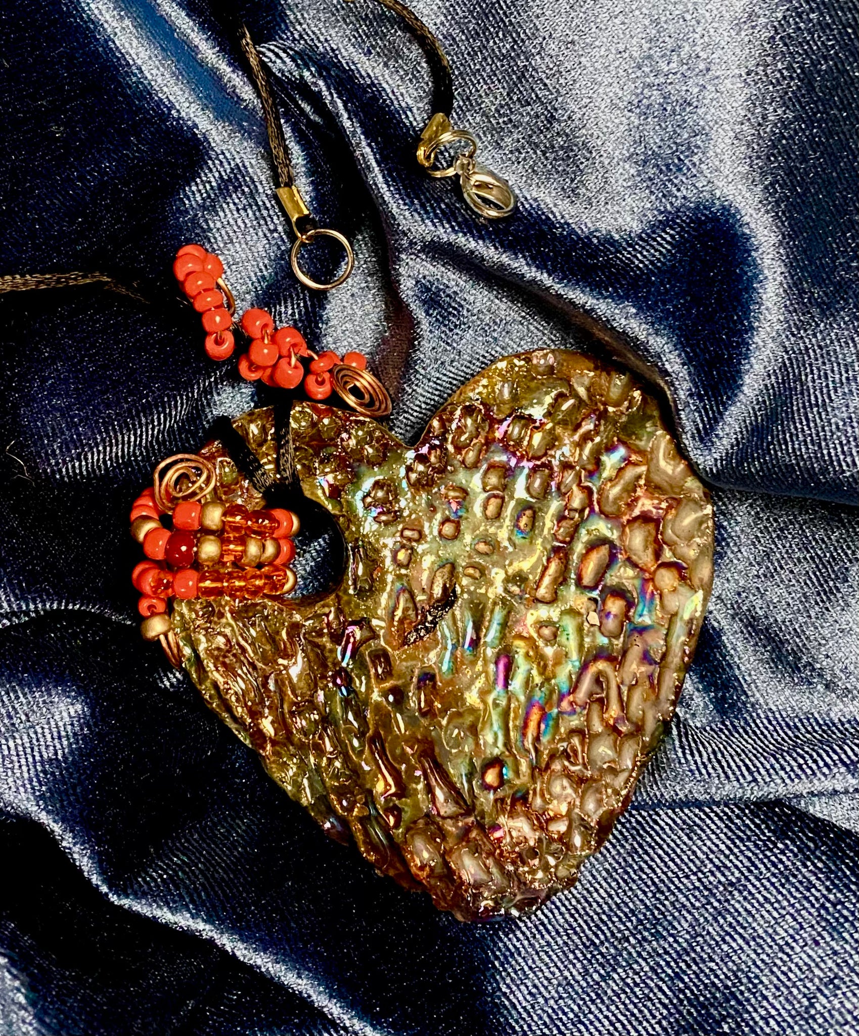  Have A Heart ! Each heart pendant is handmade with love! It is 3"x 3" and weighs approx. 3ozs. This pendant has a copper gold metallic raku glazes that renders a unique translucent  patina. The heart has a textured pattern . It holds a spiral of amber and red mini beads on a spiral copper wire. This pendant has a nice 12" black suede cord!