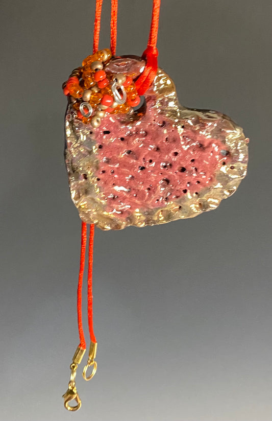 Have A Heart ! Each heart pendant is handmade with love! It is 3"x 3" and weighs approx. 3ozs. This pendant has a red violet and gold metallic raku glazes that renders a unique translucent  patina. The heart has a textured pattern . Both sides are  are different and equally beautiful! It holds a spiral of red and gold mini beads on a spiral copper wire. This pendant has a nice 12" red rattail cord!