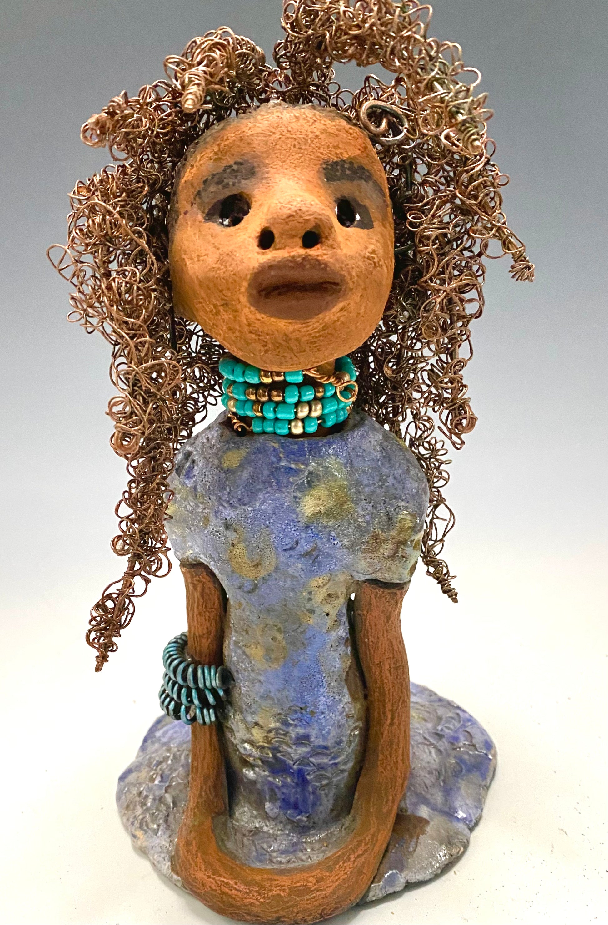 Meet Janae'! She has grown a head full of Hair! Janae' stands 8" x 5" x 4" and weighs 1.03 lbs. She has a lovely honey brown complexion with lovely reddish brown lips. Janae' wears a clay braided hairstyle. Janae' has a colorful metallic blue and gold glazed dress. She wears a blue and antique copper  beaded necklace. With eyes wide opened, Janae' has hopes of finding a new home.  