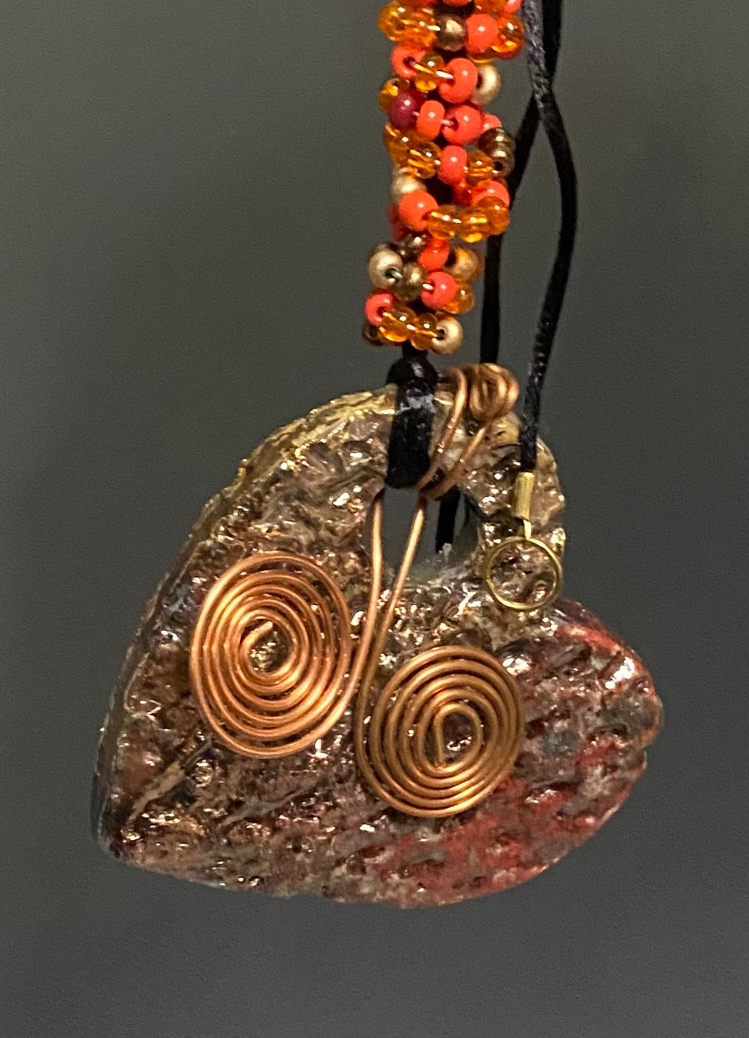 Have A Heart! Each heart pendant is handmade with love! It is 3"x 3"and weighs approx. 3ozs. This pendant has a copper and gold metallic raku glazes that renders a unique translucent  patina. The heart has a textured pattern . Both sides are  are different and equally beautiful! It holds a spiral of orange mini beads on a spiral copper wire. This pendant has a nice12" black rattail cord!