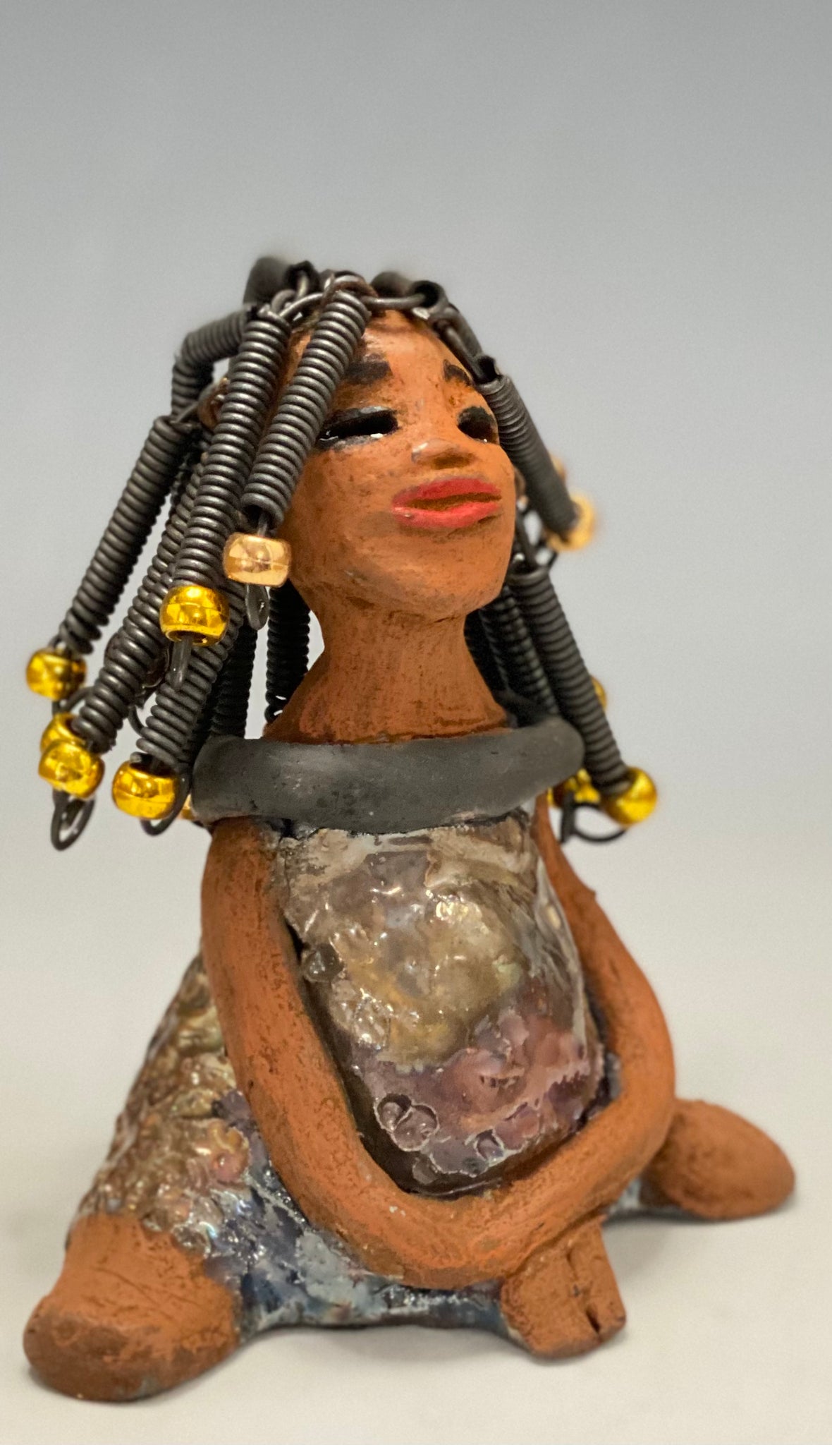   Meet Sadie  Sadie stands 5.5" x 4" x 3" and weighs 8.7 ozs. She wears a lovely glossy  metallic gold dress.. Sadie has over15 feet of coiled wire hair. Sadie appears to sit in a yoga pose. Her long arms rest at her side. Sadie is a great starter piece from the Herdew Collection!