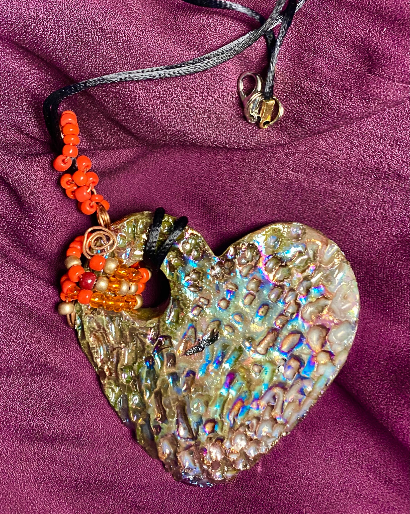  Have A Heart ! Each heart pendant is handmade with love! It is 3"x 3" and weighs approx. 3ozs. This pendant has a copper gold metallic raku glazes that renders a unique translucent  patina. The heart has a textured pattern . It holds a spiral of amber and red mini beads on a spiral copper wire. This pendant has a nice 12" black suede cord!