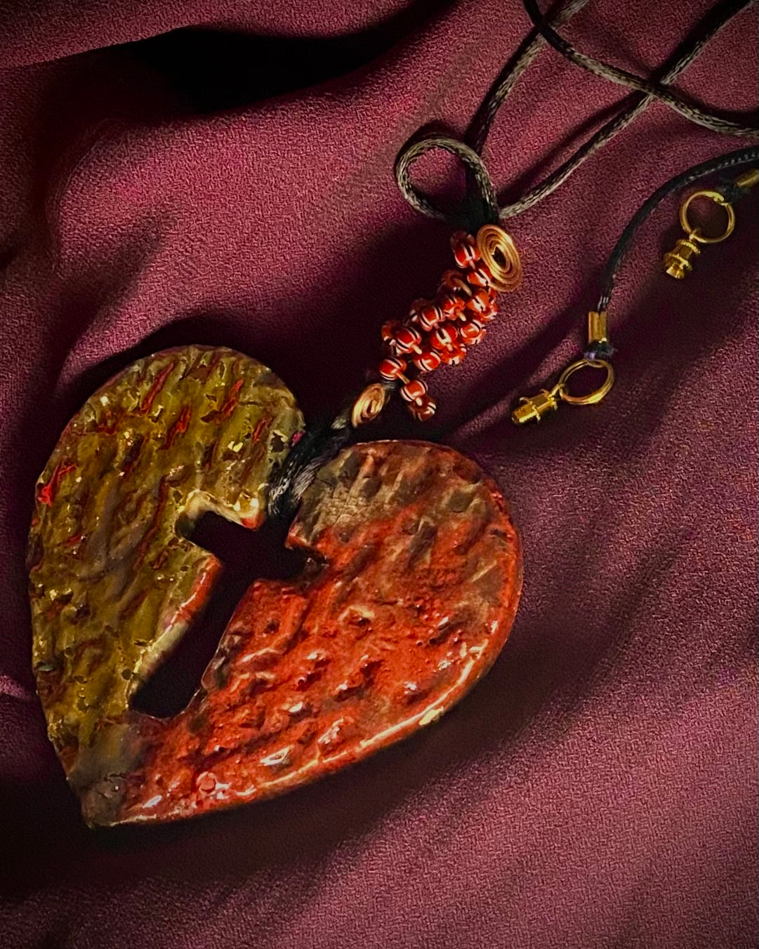 Have A Heart ! Each heart pendant is handmade with love! It is 3"x 3" and weighs approx. 3ozs. This pendant has a red and gold metallic raku glazes that renders a unique translucent  patina. The heart is textured and has a cut out cross in the center. It holds a spiral of red and white mini beads on a spiral copper wire. This pendant has a nice 12" black suede cord!